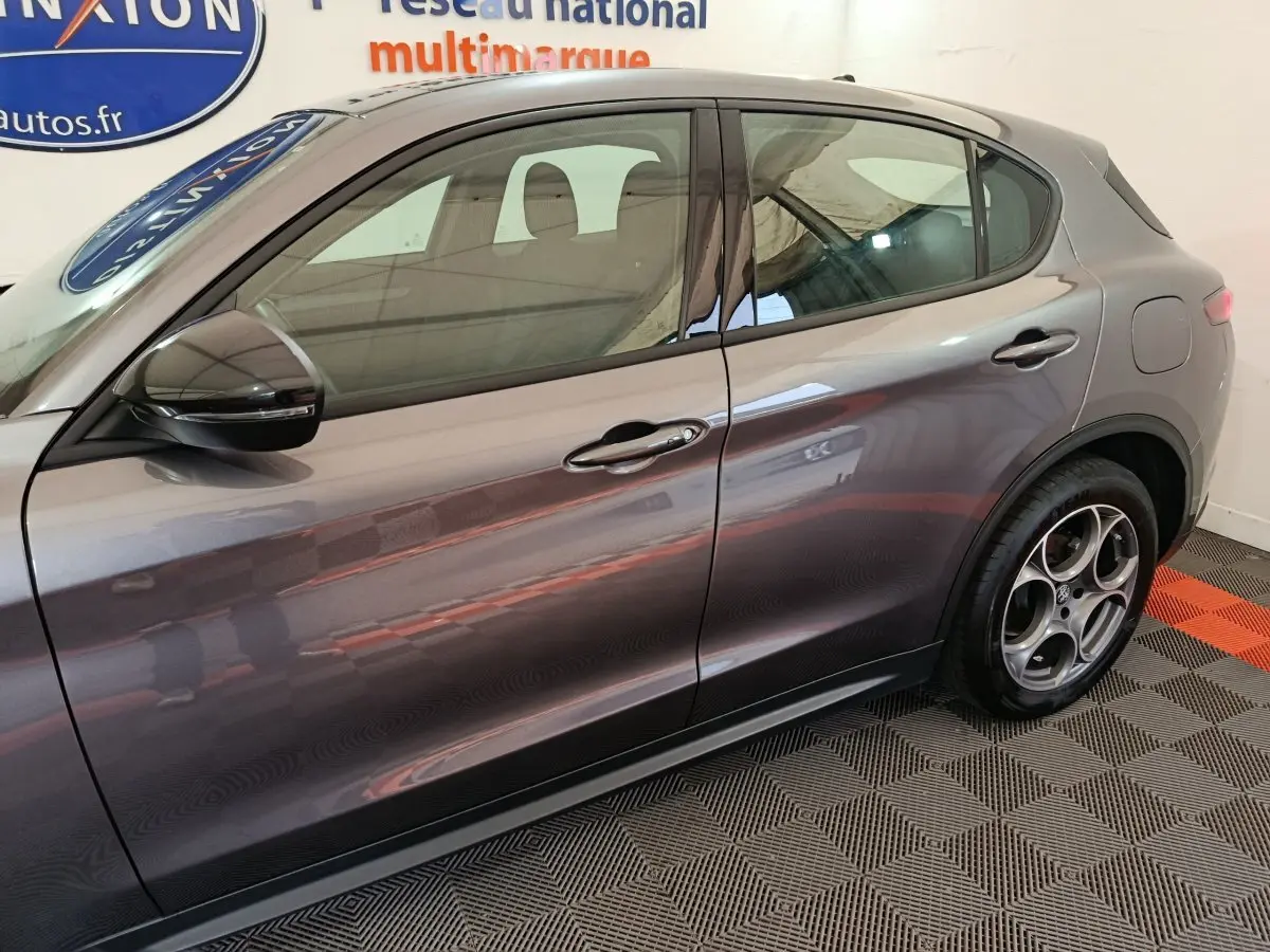 Vue latérale droite d'un Alfa Romeo Stelvio gris foncé, mettant en valeur les jantes distinctives et les lignes élégantes du SUV.