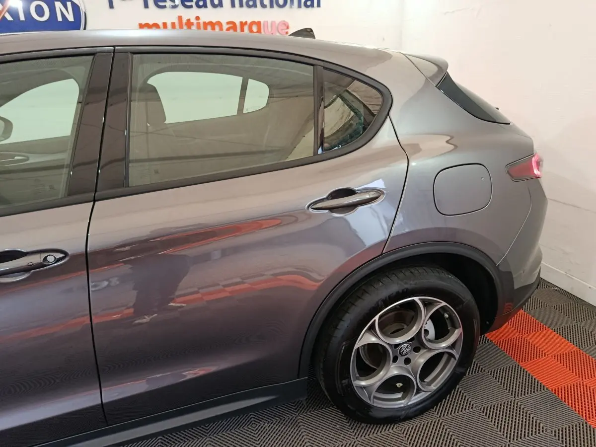 Vue latérale droite sur l'arrière d'un Alfa Romeo Stelvio gris foncé avec jante alliage distinctive et feu arrière allumé.