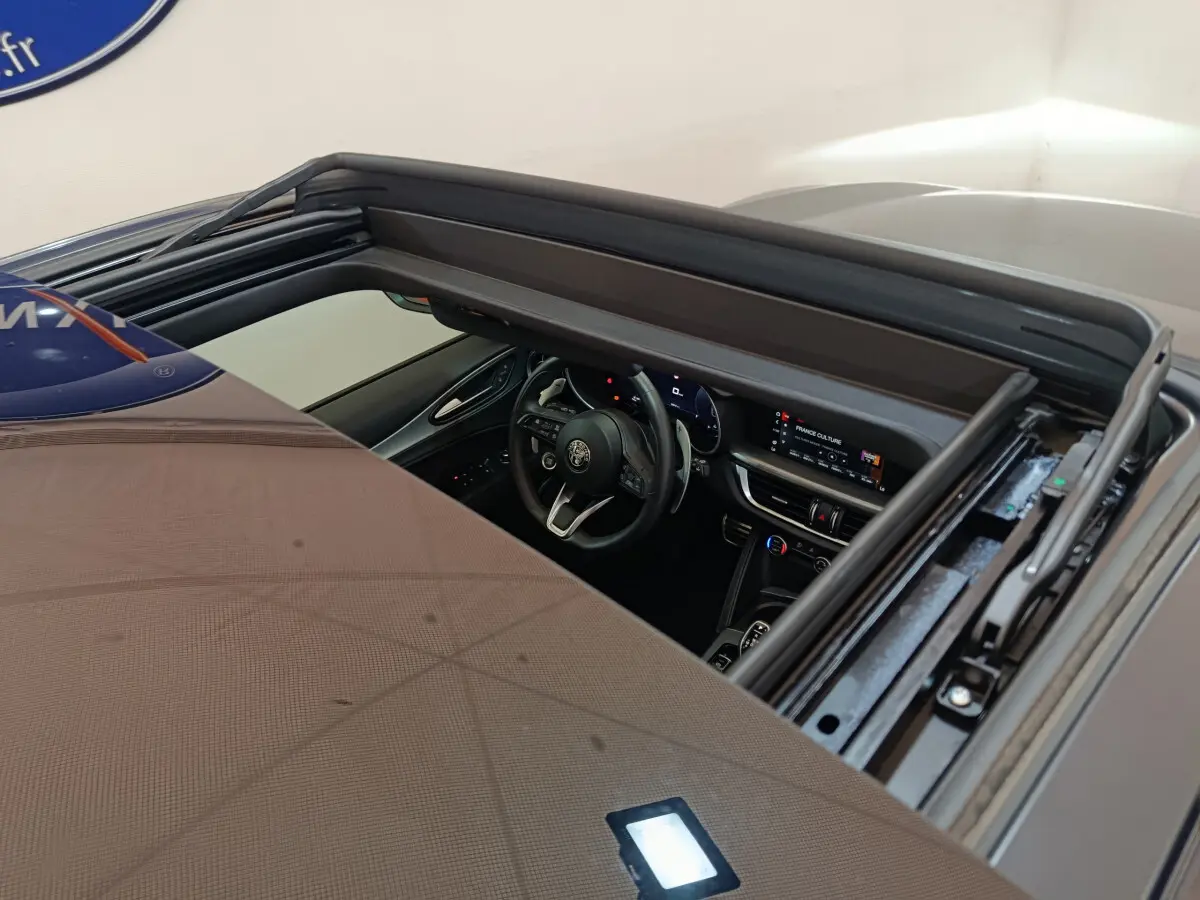 Vue plongeante sur l'intérieur noir d'un Alfa Romeo Stelvio gris foncé 2024, avec tableau de bord et volant visibles.