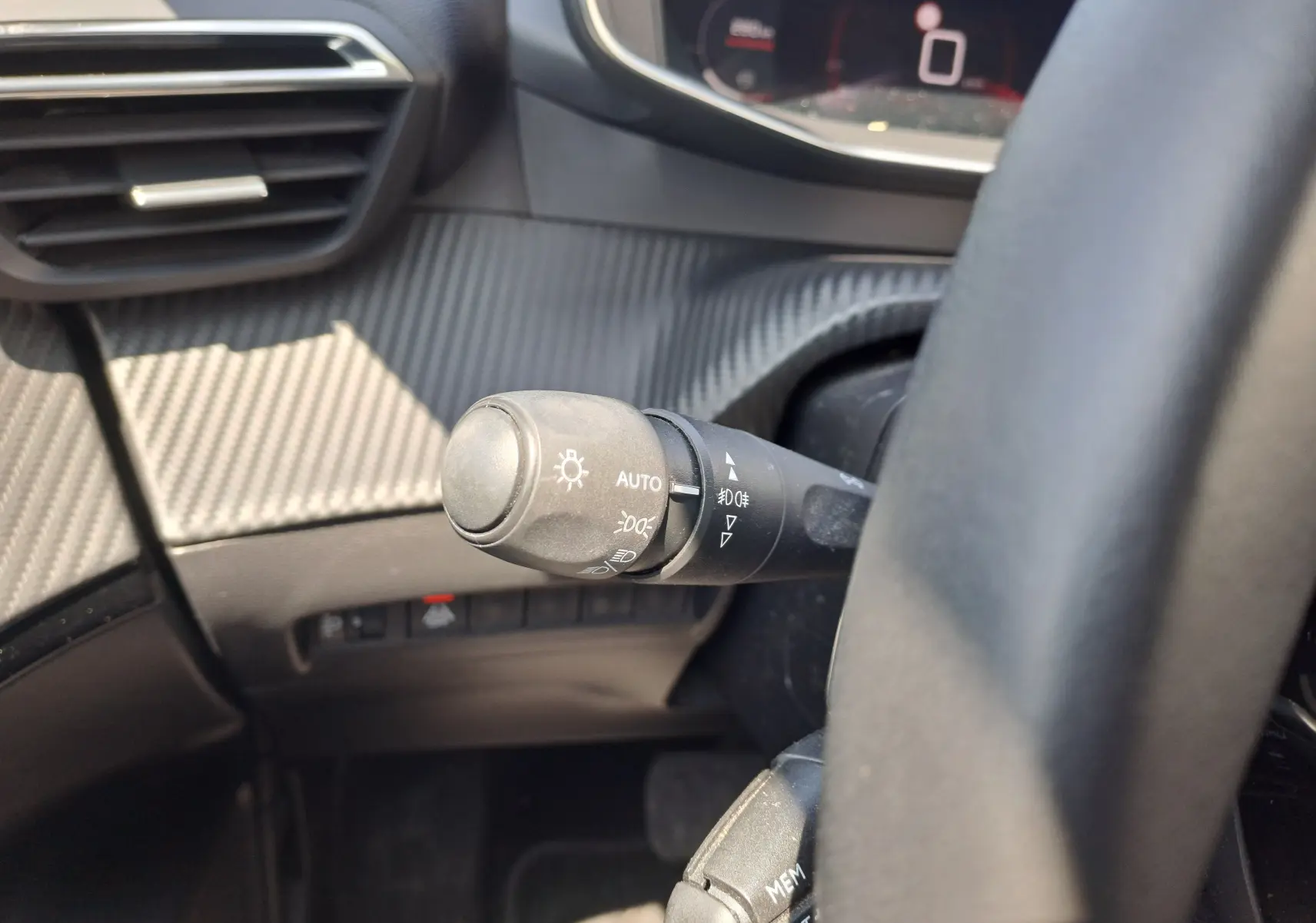 Gros plan sur la commande d'éclairage à gauche du volant dans l'habitacle noir du Peugeot 2008 rouge 2021.