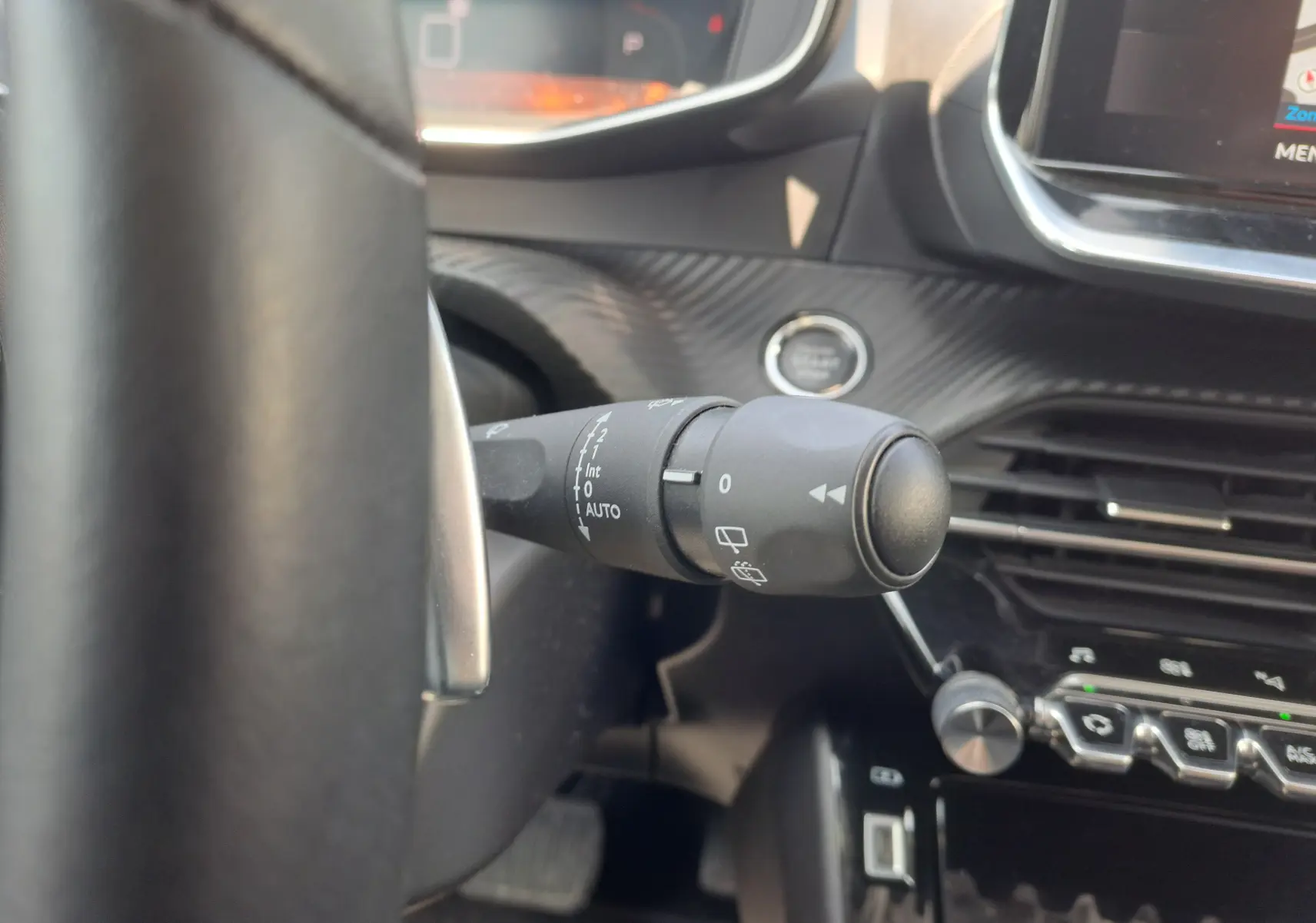 Gros plan sur la commande d'essuie-glace à gauche du volant dans l'habitacle noir du Peugeot 2008 rouge 2021.