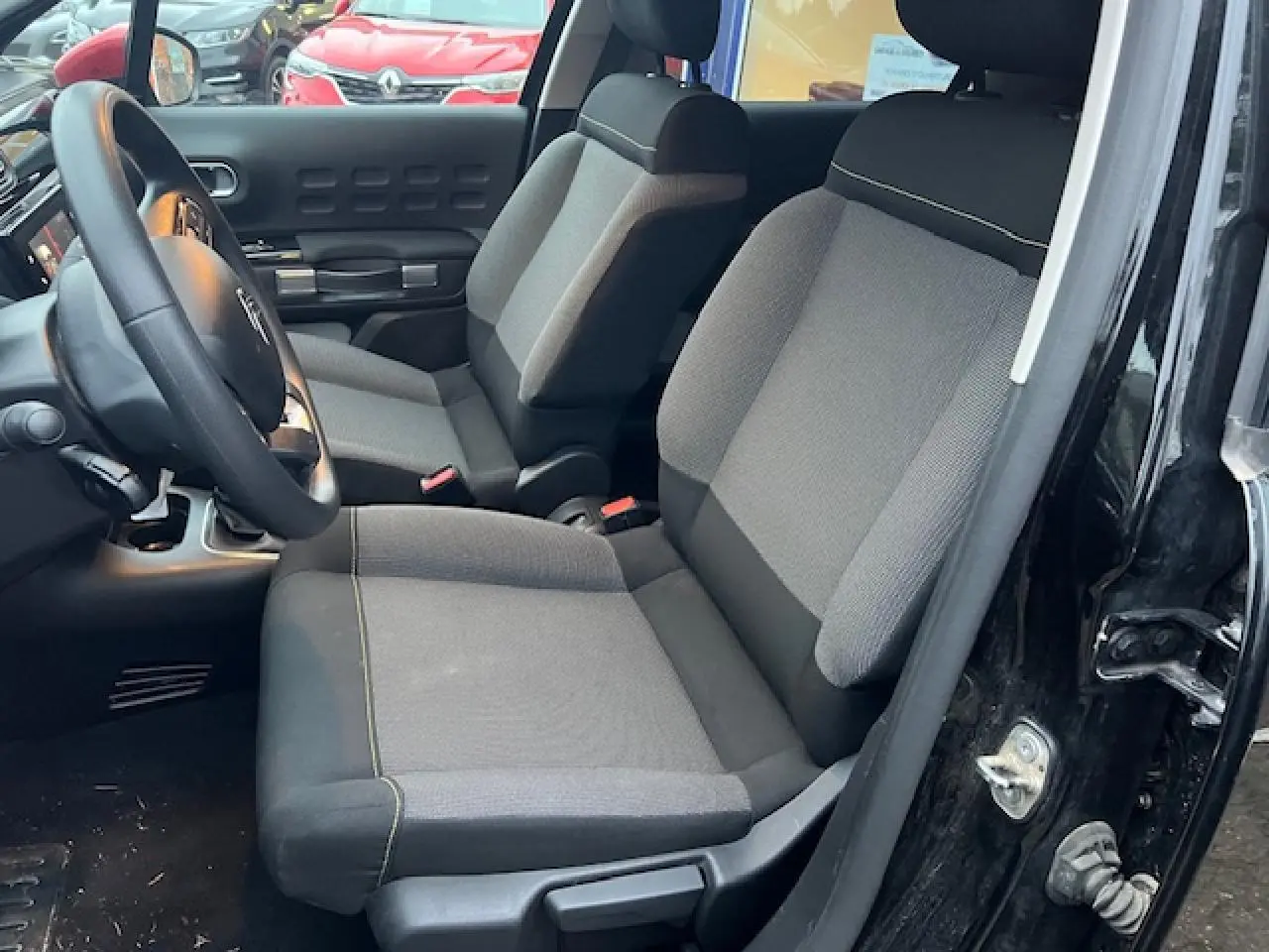 Vue intérieure côté conducteur de la Citroën C3 Shine 2023 noire toit rouge, sièges tissu gris et tableau de bord visible.