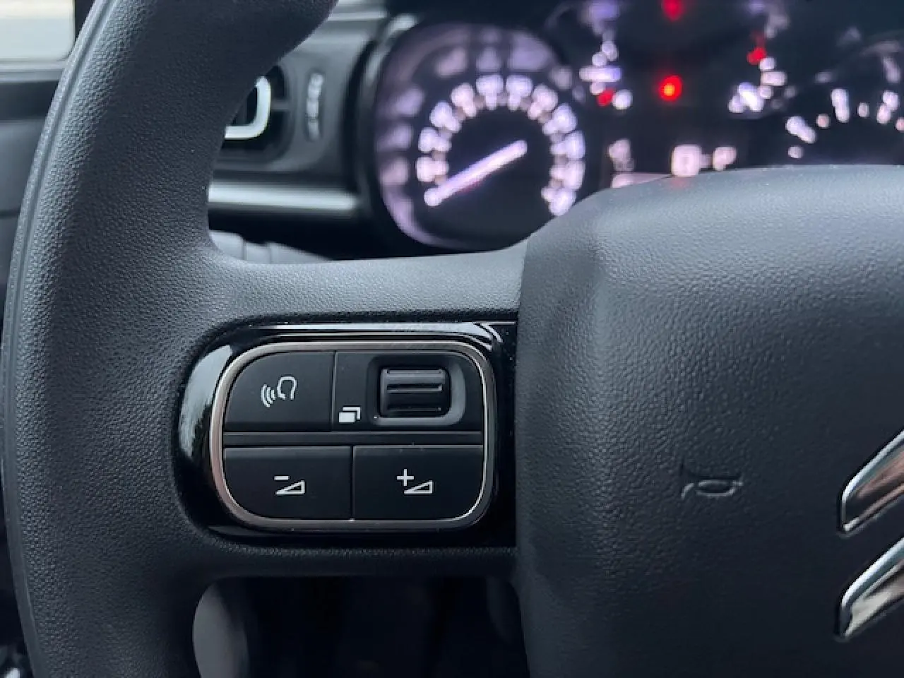 Gros plan sur les commandes audio au volant d'une Citroën C3 Shine 2023, volant noir avec logo chrome partiel visible.