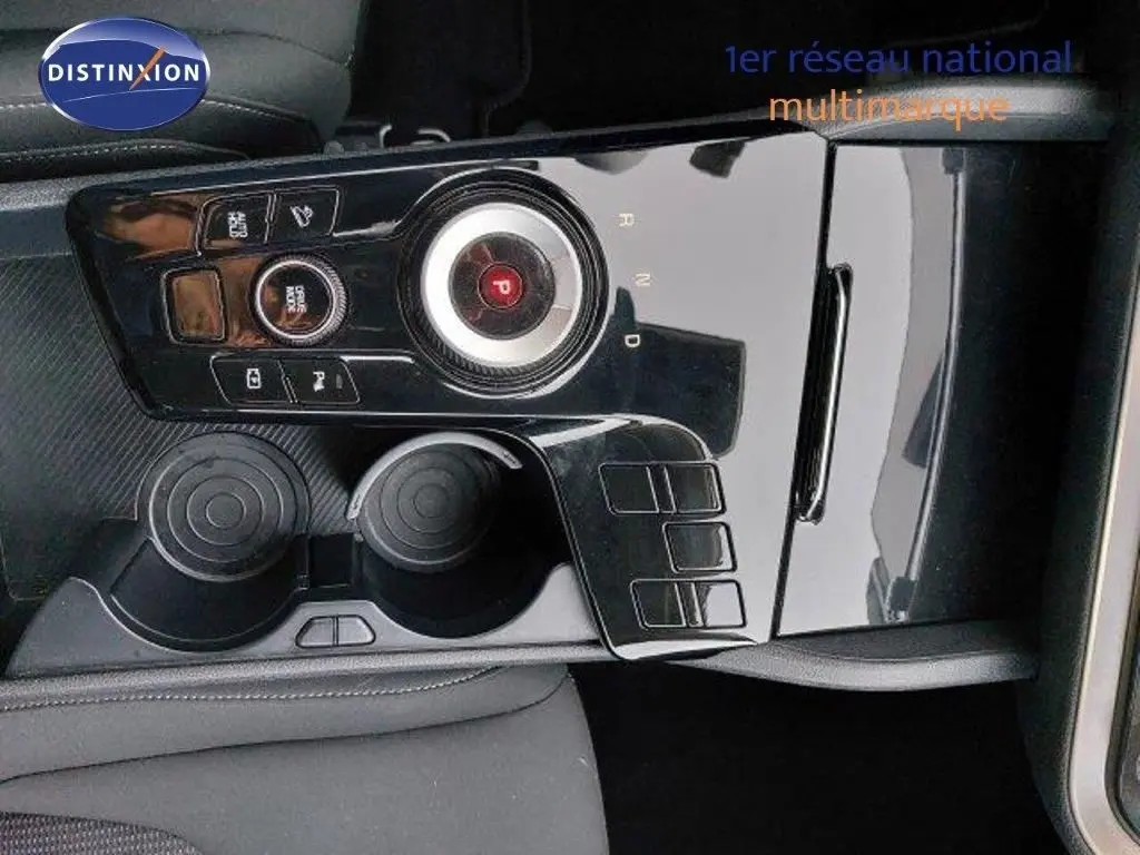 Gros plan sur la console centrale noire brillante du Kia Sportage 2024, avec molette de sélection de vitesse et porte-gobelets.