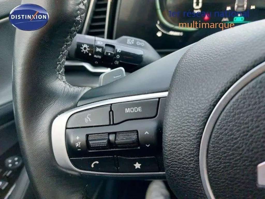 Gros plan sur les commandes au volant cuir noir du Kia Sportage 2024 hybride, avec les boutons de mode et volume visibles.