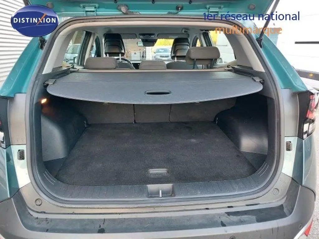 Coffre ouvert vu de l'arrière du Kia Sportage gris Sirius Metal 2024, avec cache-bagages déployé et intérieur spacieux.