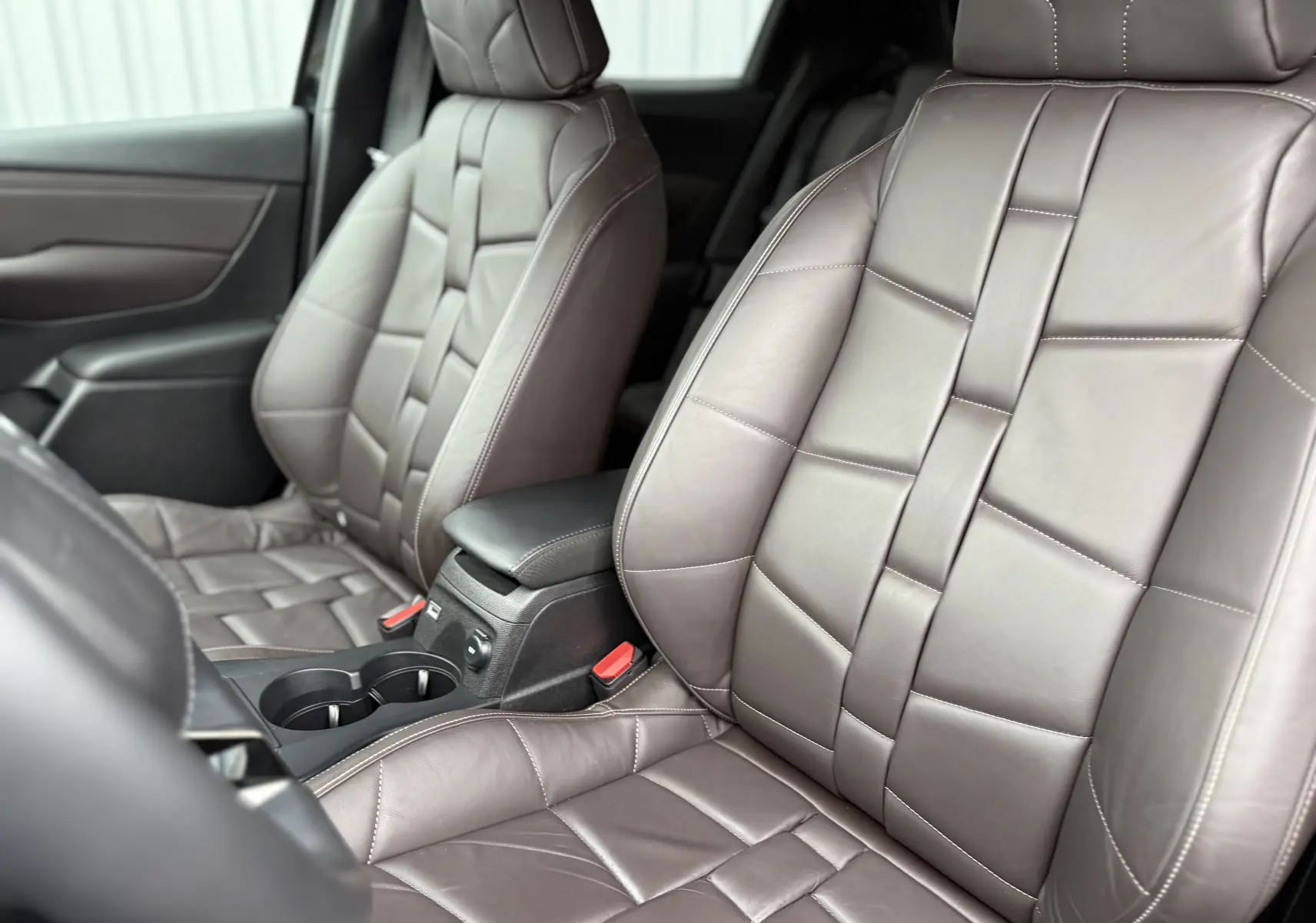 Gros plan sur les sièges avant en cuir marron du DS3 2024, mettant en valeur leur design tressé et la console centrale noire.