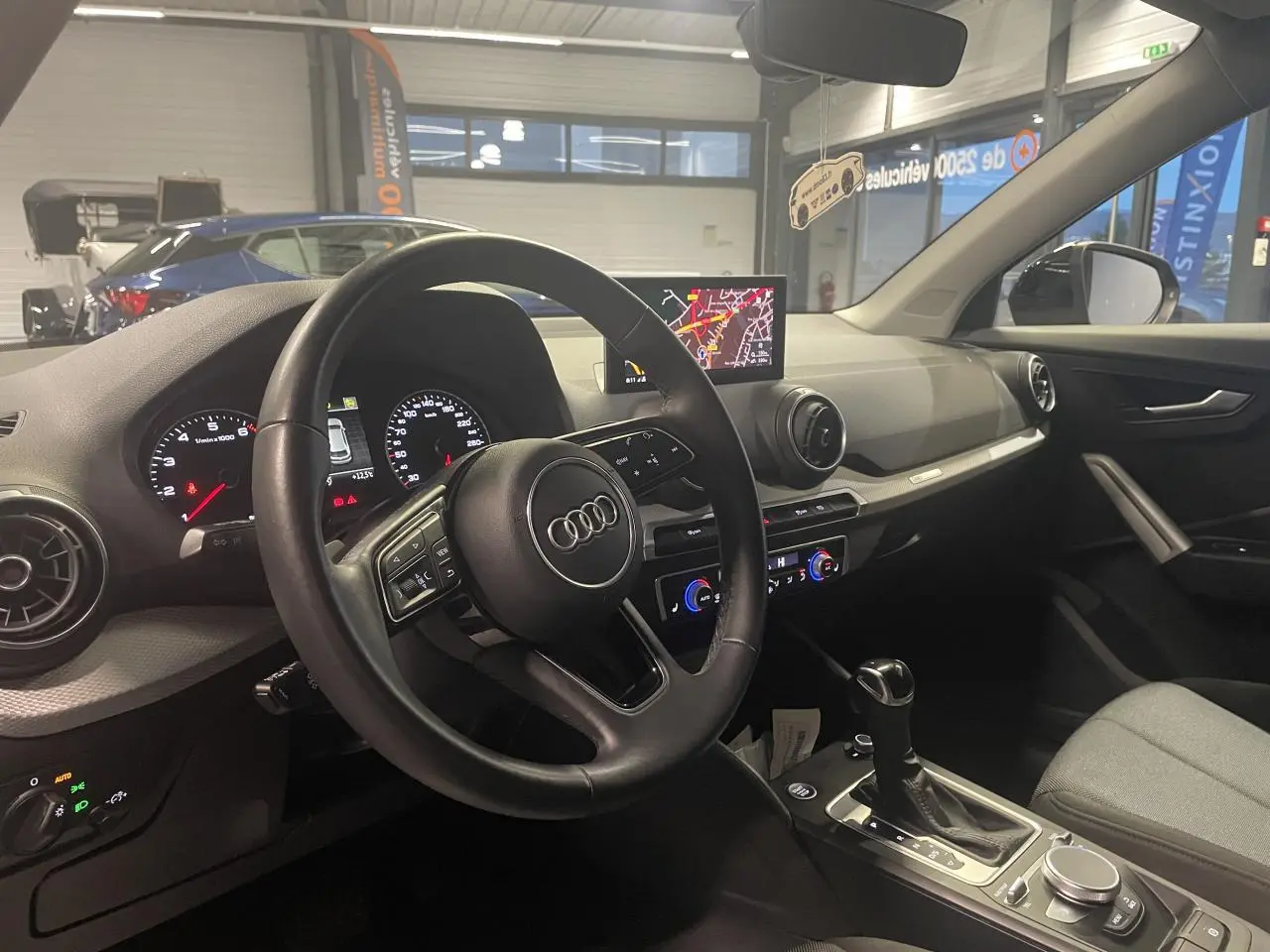 Vue intérieure côté conducteur de l'Audi Q2 2023, volant cuir S line, tableau de bord avec écran navigation et commandes digitales.