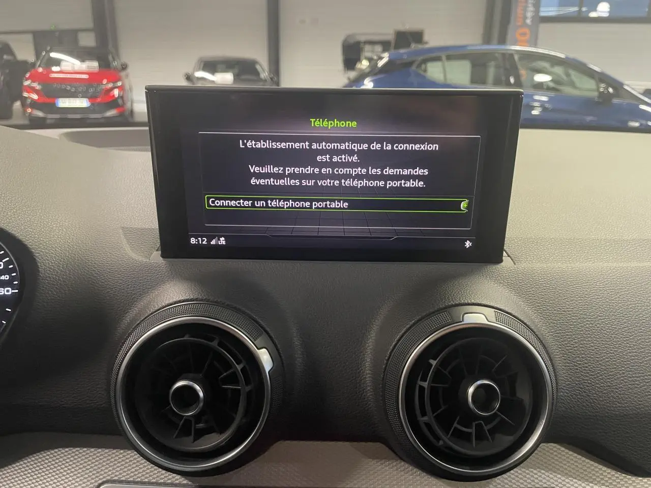 Vue intérieure du tableau de bord de l'Audi Q2 2023, écran central affichant la connexion téléphone, aérateurs ronds noirs.