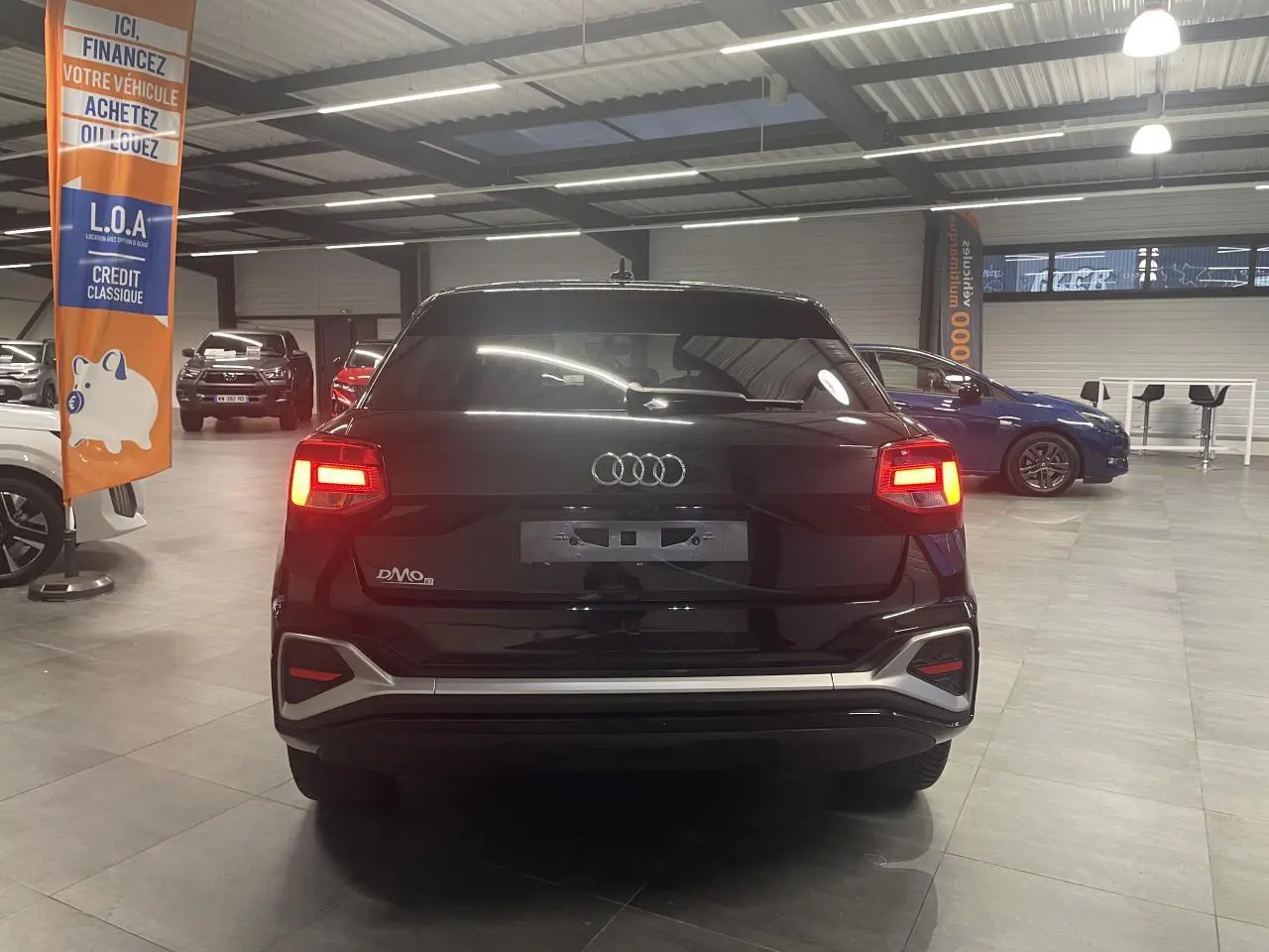 Vue arrière d’un Audi Q2 noir métallisé 2023 avec feux arrière allumés dans un showroom.