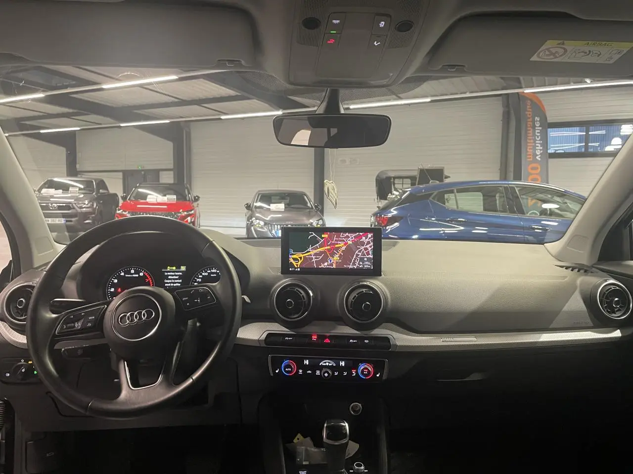 Vue intérieure avant de l'Audi Q2 2023, tableau de bord noir avec écran navigation et volant multifonction S line.