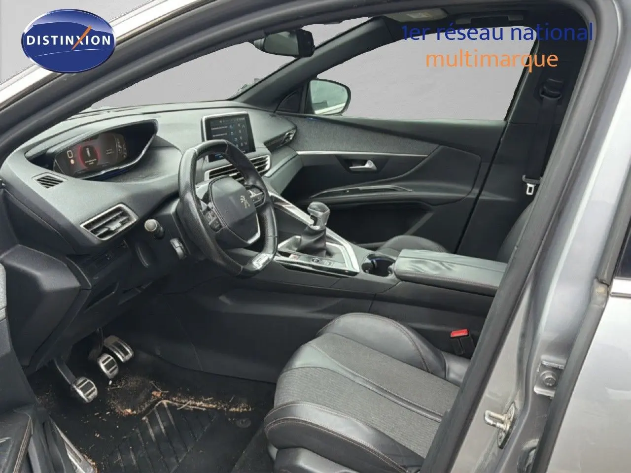Vue intérieure côté conducteur d’un Peugeot 5008 gris Artense, avec volant compact et levier de vitesse manuel visible.