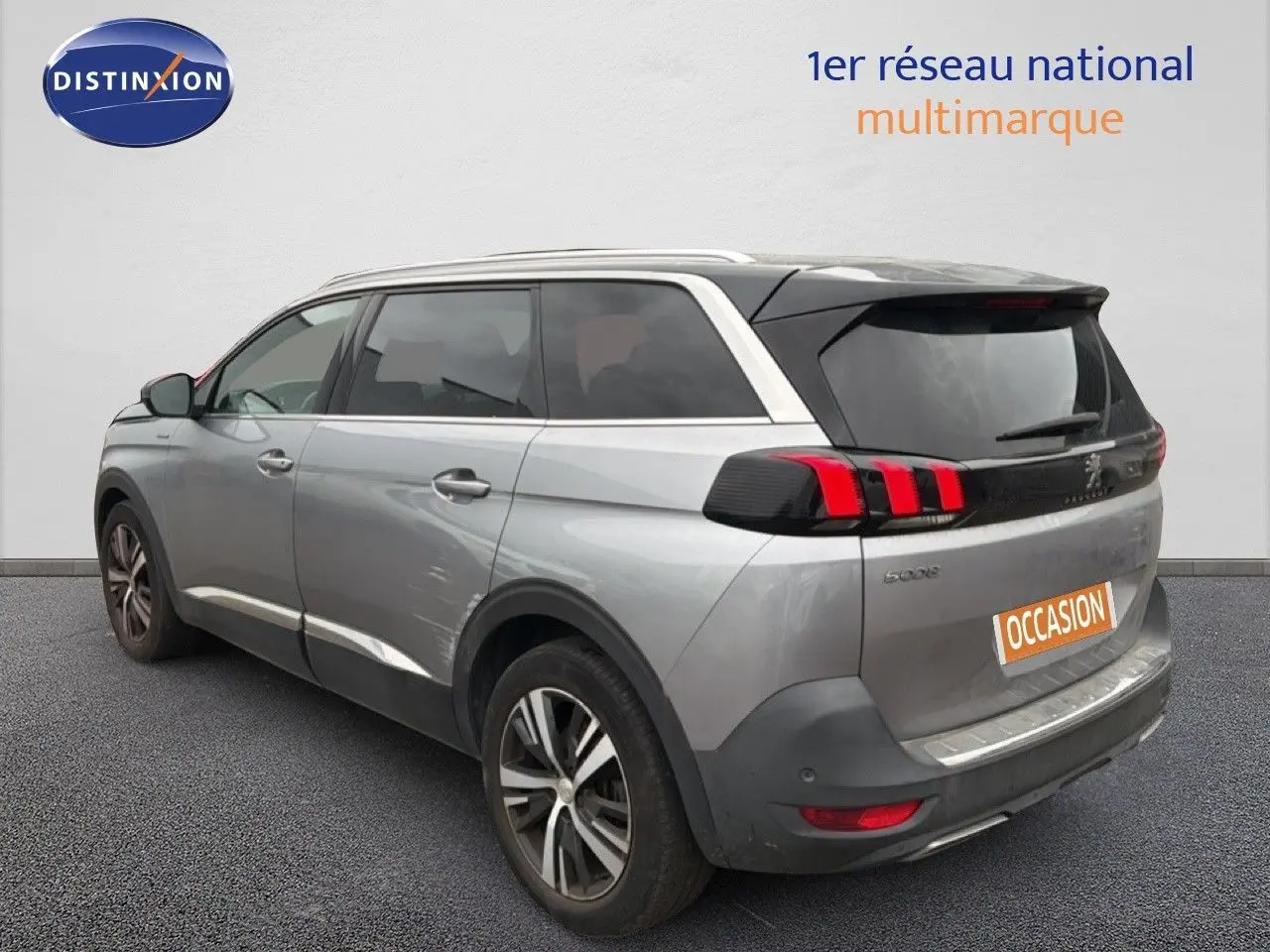 Vue 3/4 arrière droite d'un Peugeot 5008 gris Artense avec feux arrière à griffes rouges et jantes alliage bicolores.