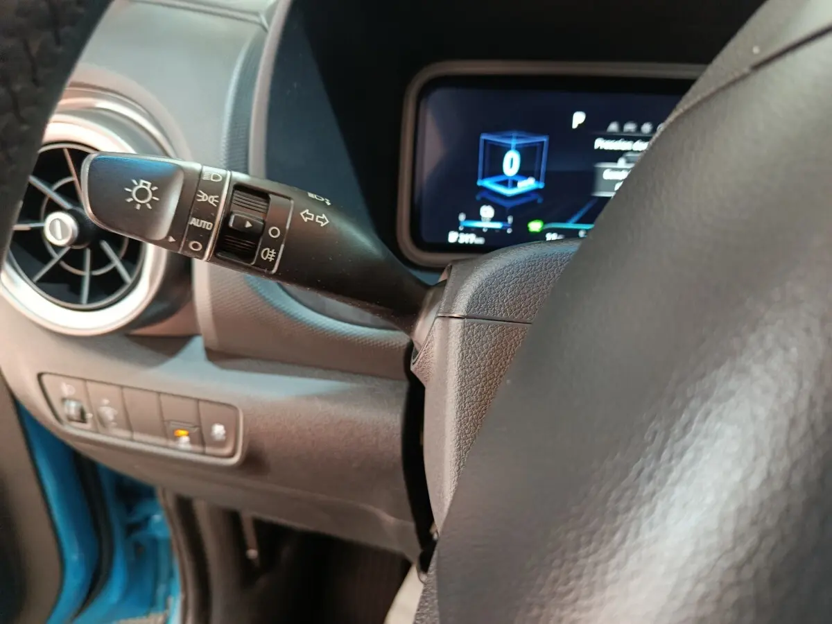 Gros plan sur la manette de commande des phares et clignotants du tableau de bord d’une Hyundai Kona électrique bleue.
