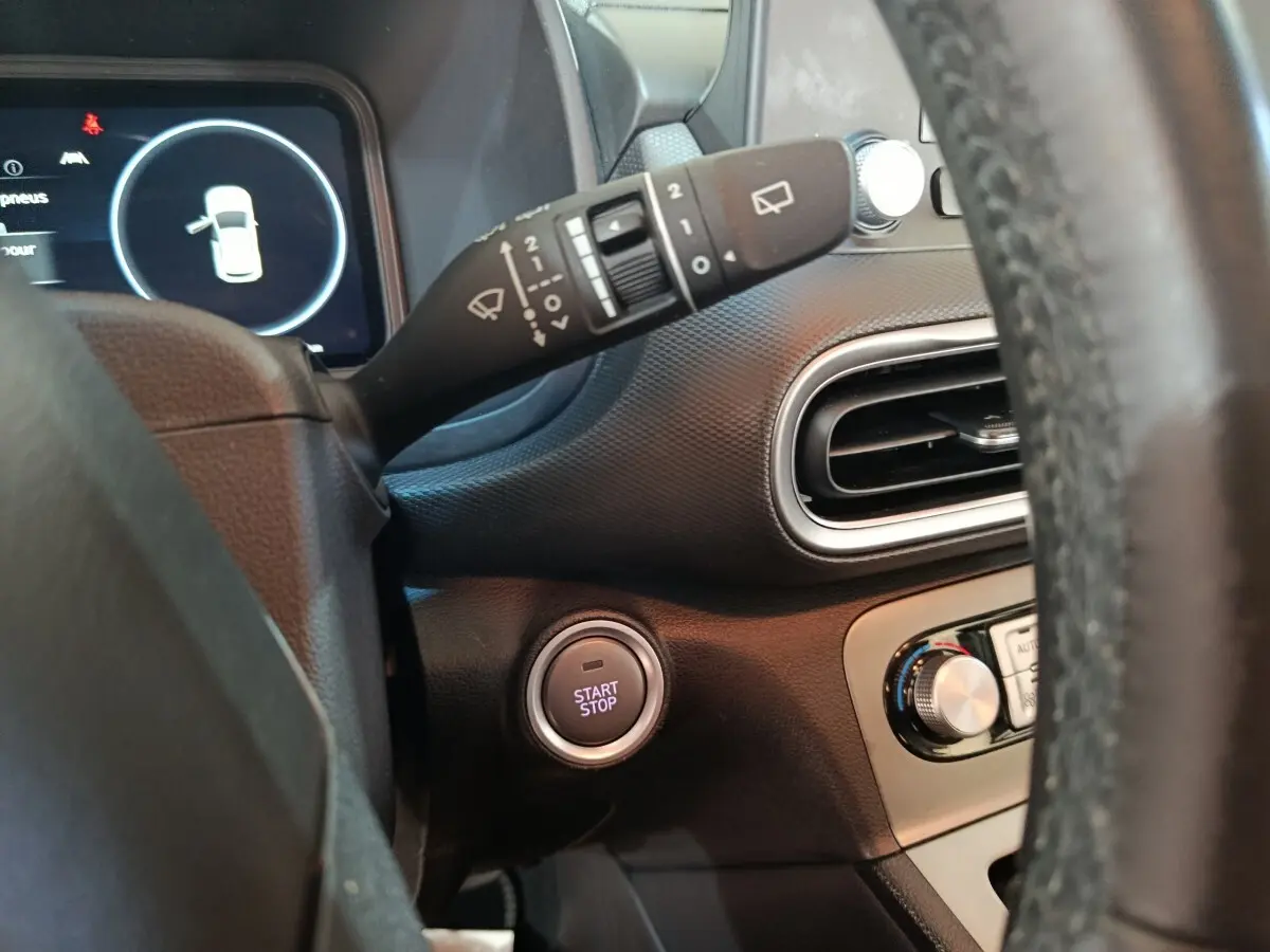 Vue intérieure côté gauche du tableau de bord du Hyundai Kona bleu avec bouton démarrage et commande essuie-glace.
