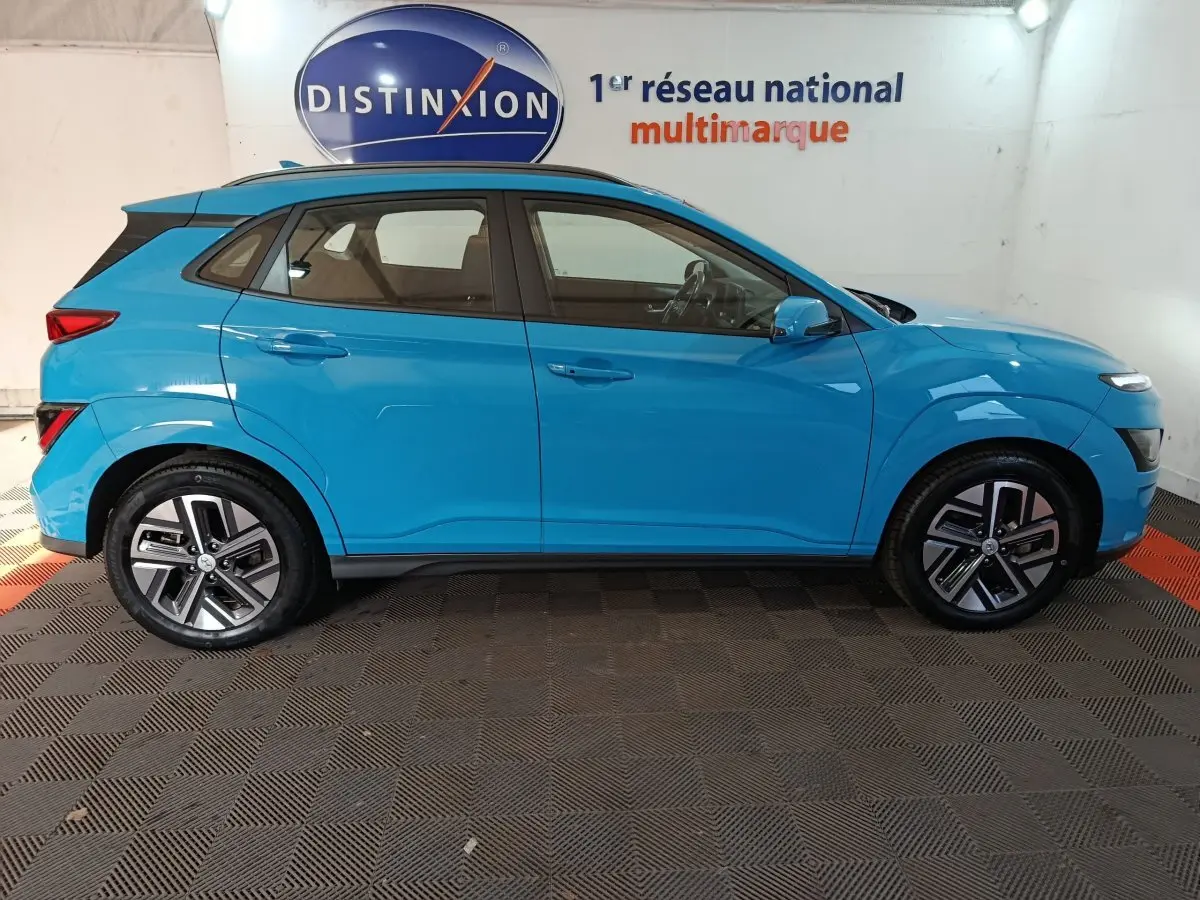 Vue de profil côté gauche d'un Hyundai Kona électrique bleu 2022 avec jantes spécifiques et toit noir contrasté.