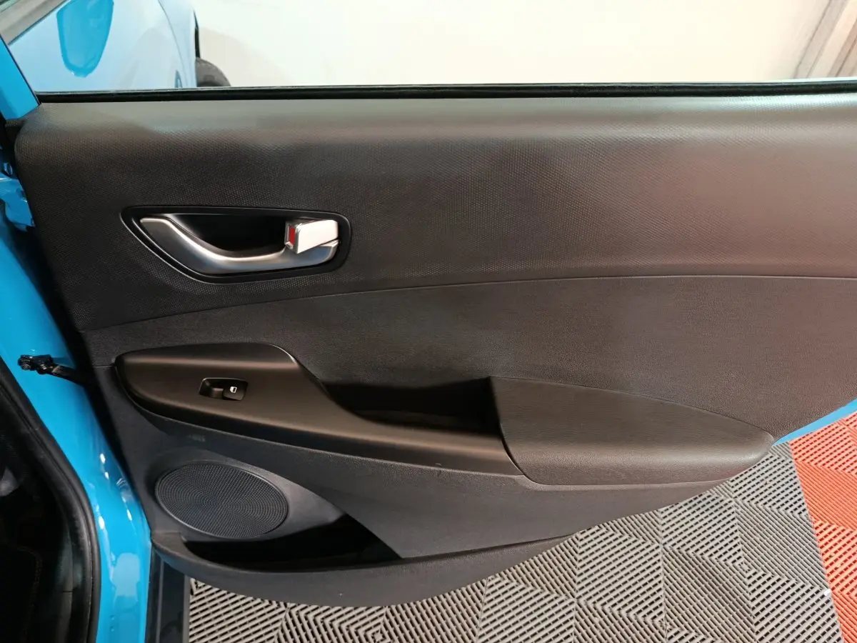 Vue intérieure de la porte avant gauche bleu électrique du Hyundai Kona BEV avec poignée argentée et commande de vitre.