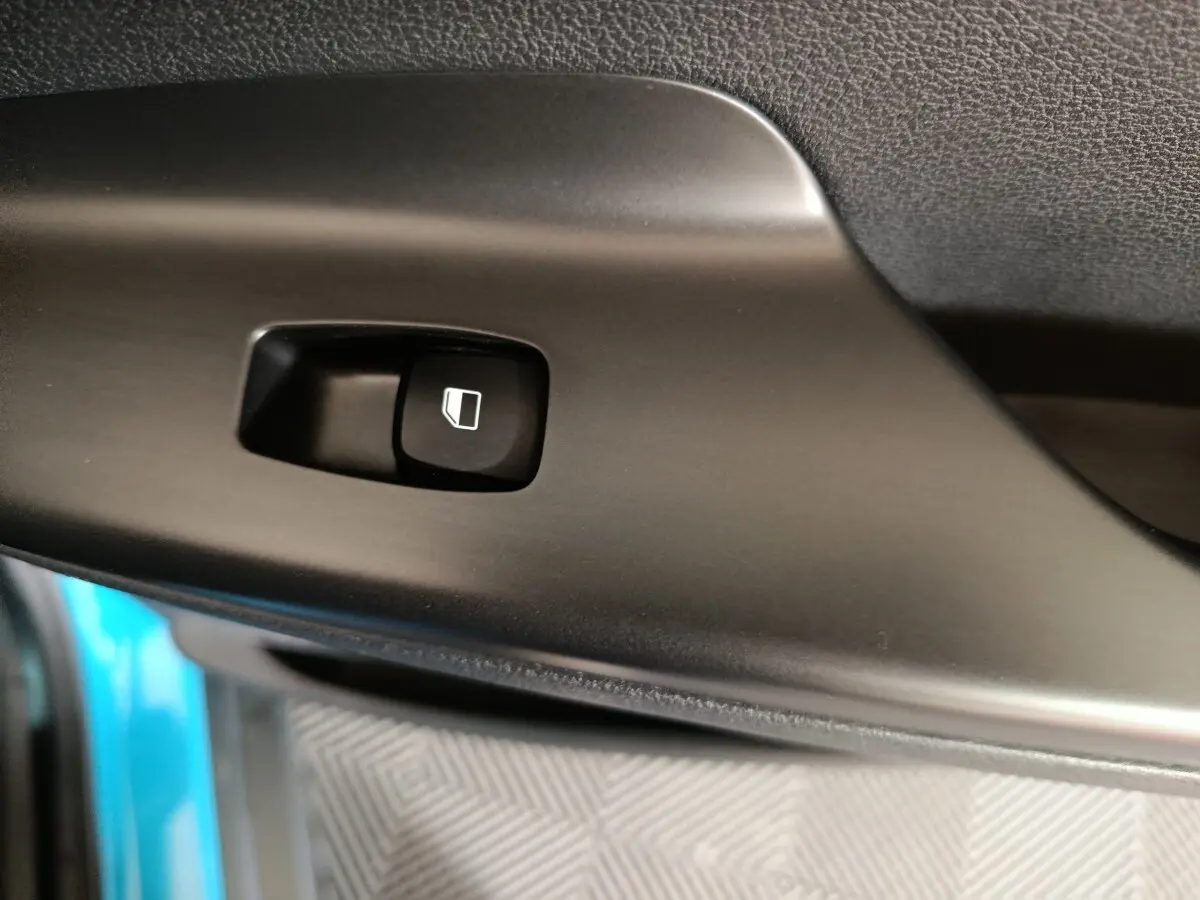 Gros plan sur le bouton de commande de vitre électrique noir dans l’habitacle d’une Hyundai Kona bleu électrique.