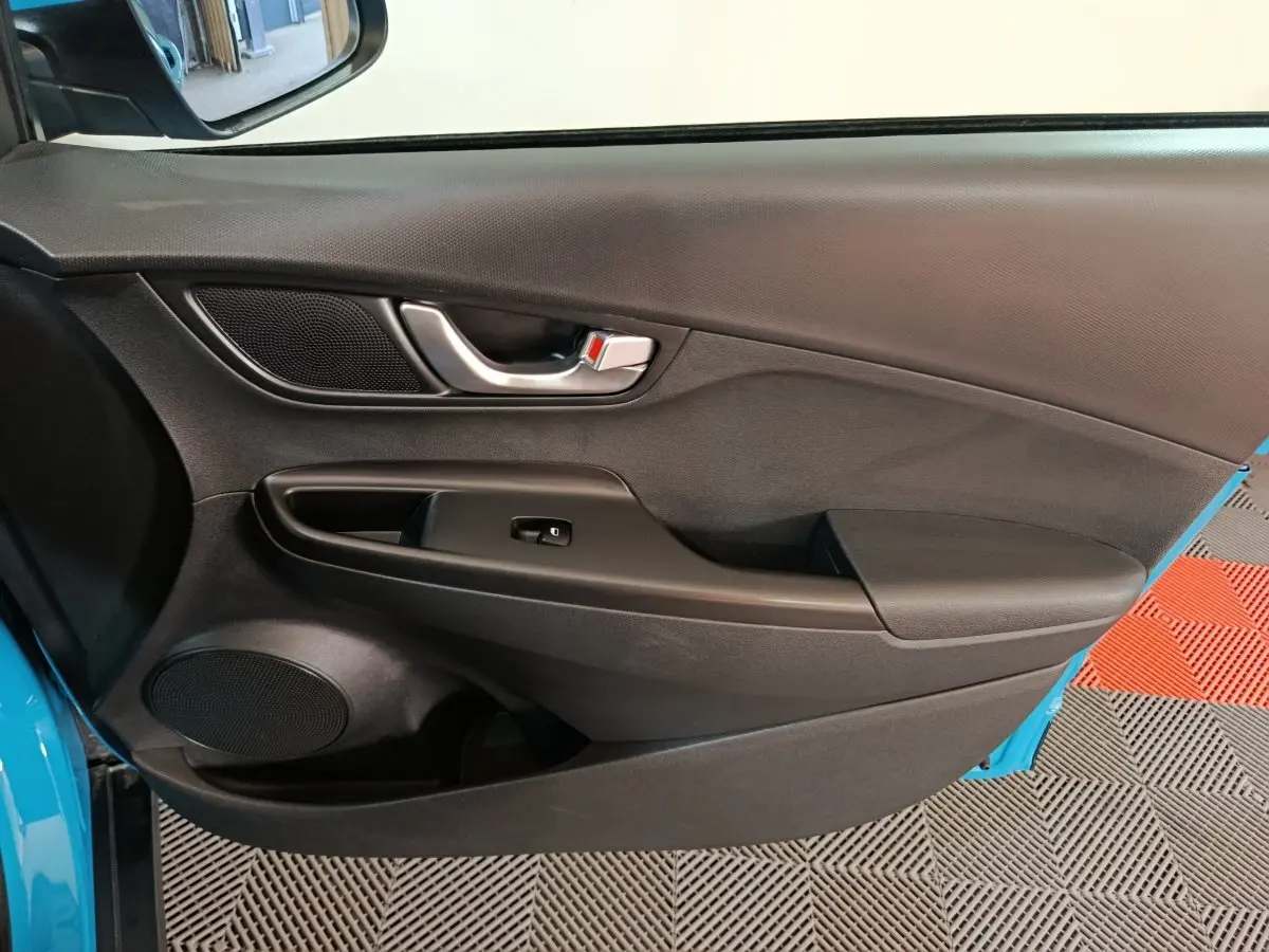 Intérieur côté conducteur de Hyundai Kona électrique bleu 2022, porte avec poignée argent et commande fenêtre noire.