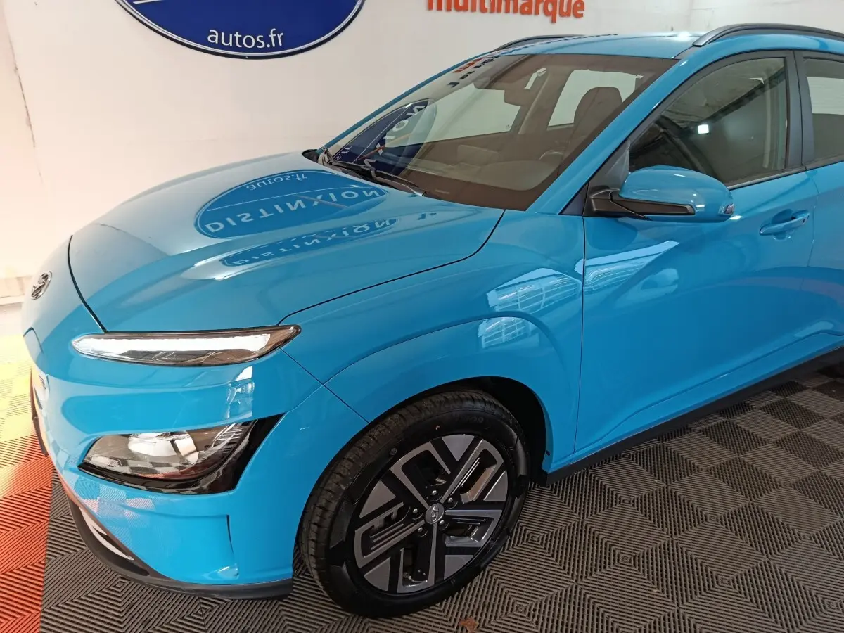 Vue 3/4 avant droit d'une Hyundai Kona électrique bleu vif avec jantes spécifiques et feux LED distinctifs.
