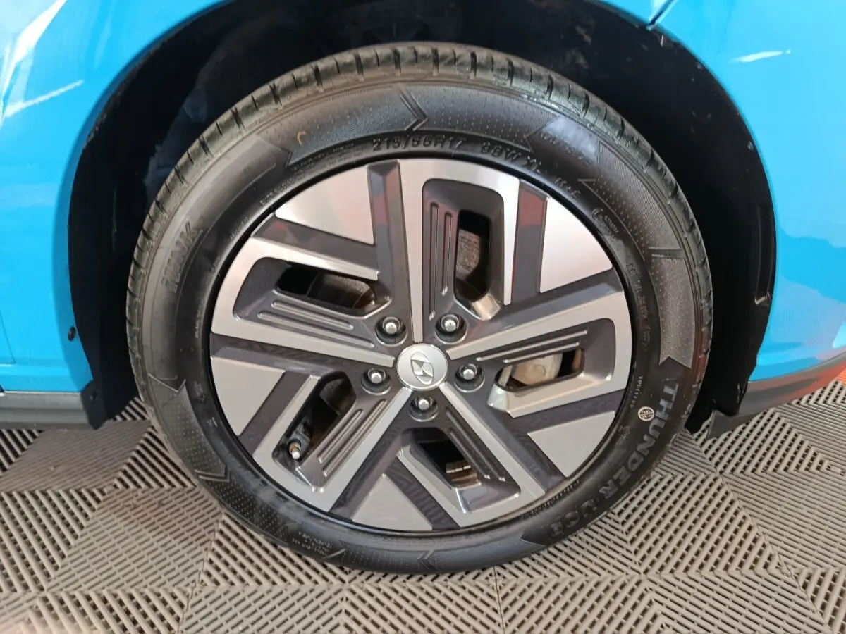 Gros plan sur la roue avant gauche du Hyundai Kona électrique bleu, mettant en valeur la jante au design moderne.