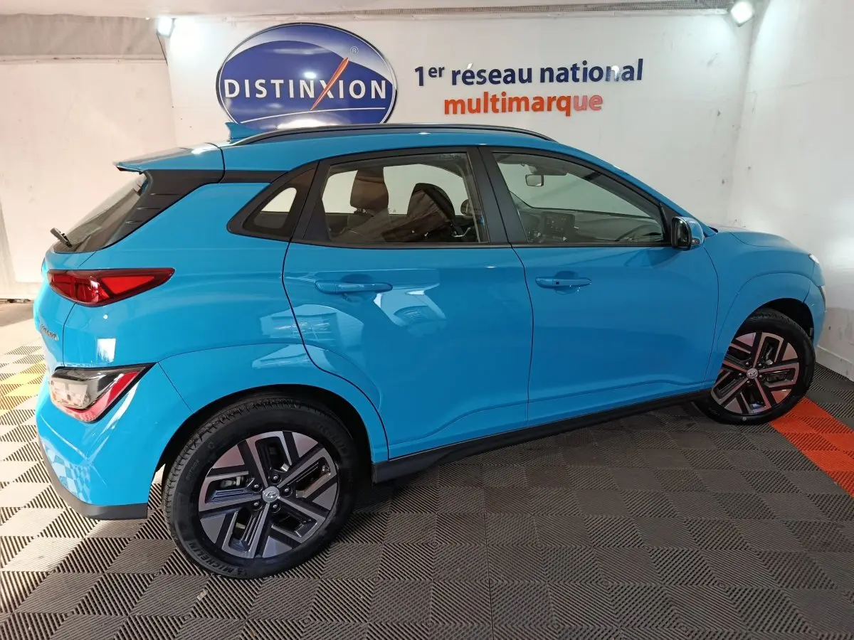 Vue de profil côté droit d'un Hyundai Kona électrique bleu 2022, avec jantes spécifiques et toit noir contrastant.