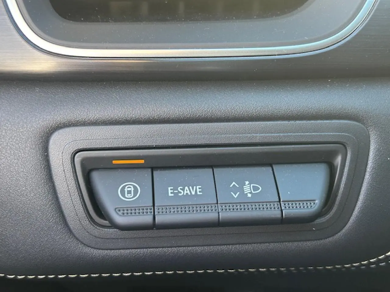 Gros plan sur les boutons de commande noirs du tableau de bord du Renault Symbioz blanc nacré, avec éclairage orange.
