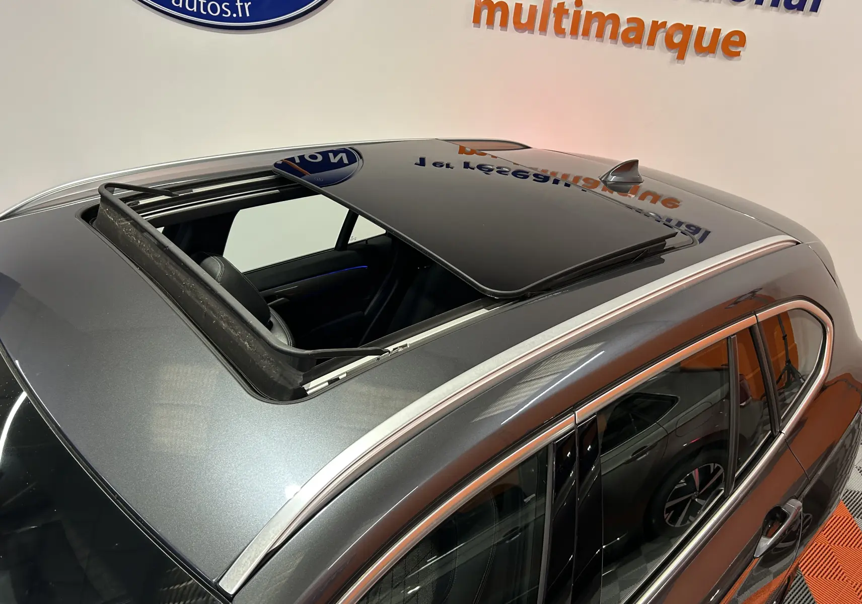 Vue plongeante sur le toit ouvrant ouvert d’un BMW X1 gris métallisé, avec détails chromés autour des vitres.