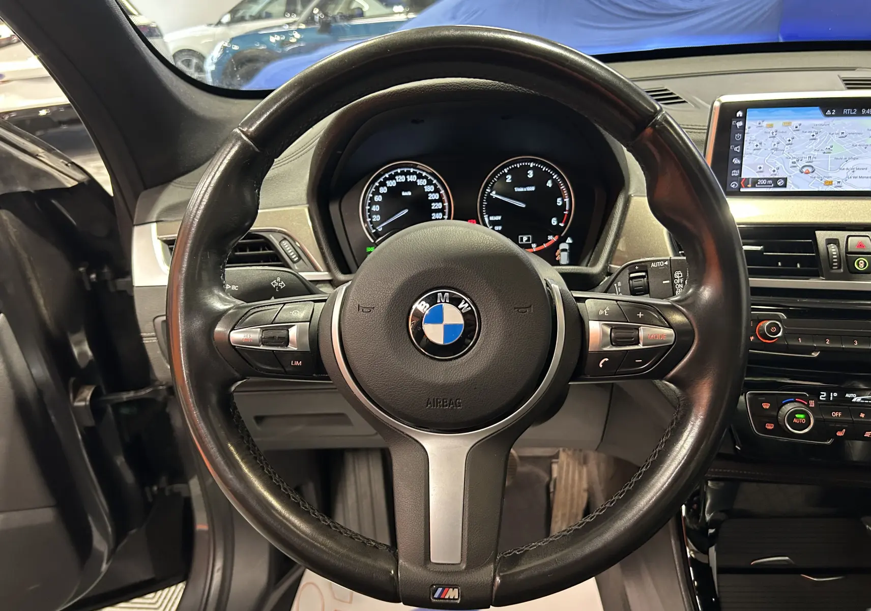 Vue intérieure centrée sur le volant cuir noir avec logo BMW et tableau de bord du BMW X1 gris de 2021.