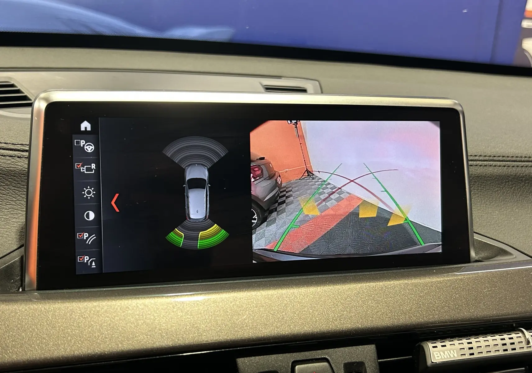 Écran central du BMW X1 gris montrant la caméra de recul et les capteurs de stationnement en fonctionnement.