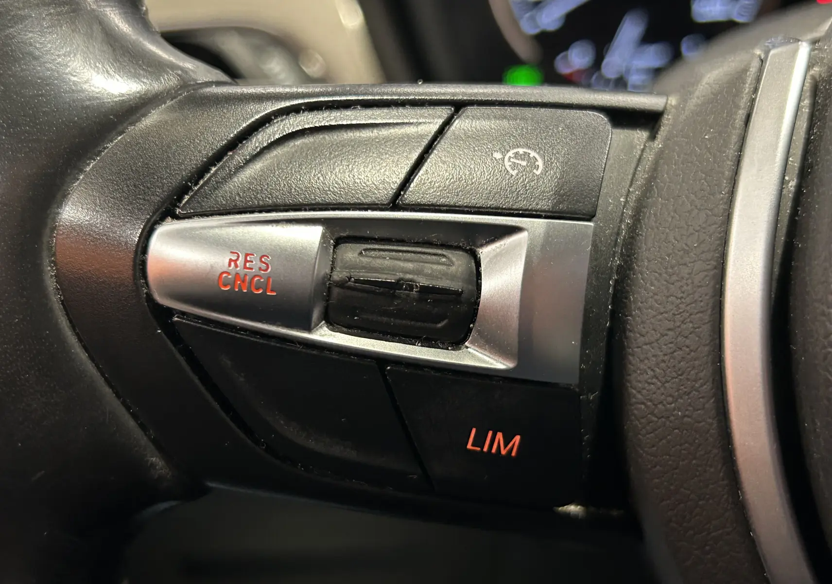 Gros plan sur les commandes de régulateur de vitesse au volant noir du BMW X1 gris, avec boutons rétroéclairés rouges.