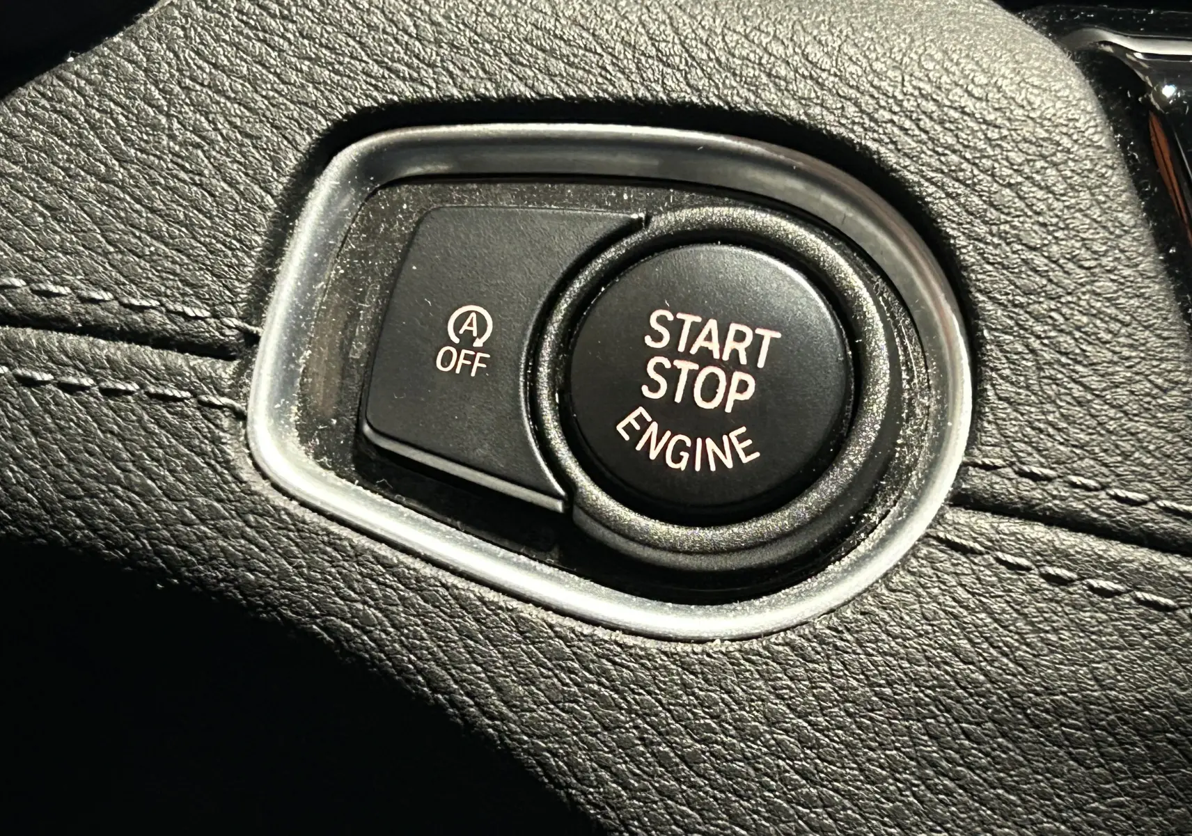 Gros plan sur le bouton Start Stop Engine et la commande Auto Start/Stop dans l'habitacle noir d'une BMW X1 gris.