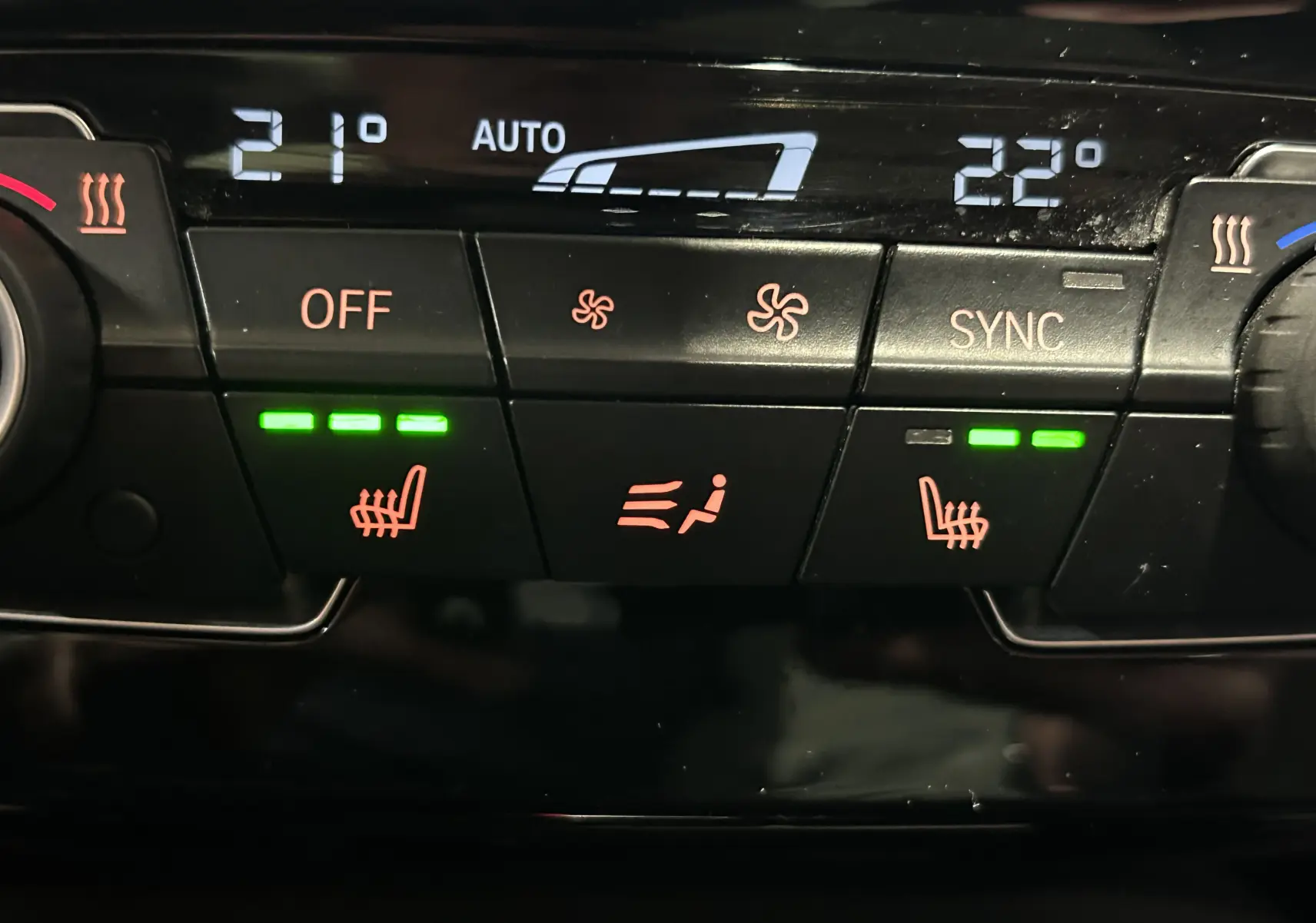 Panneau de commande de la climatisation avec sièges chauffants activés, affichage digital et boutons rétroéclairés dans une BMW X1 gris.