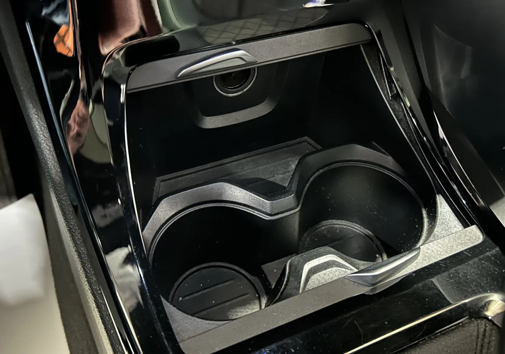 Gros plan sur les porte-gobelets noirs et la console centrale brillante d’un BMW X1 gris, intérieur moderne.