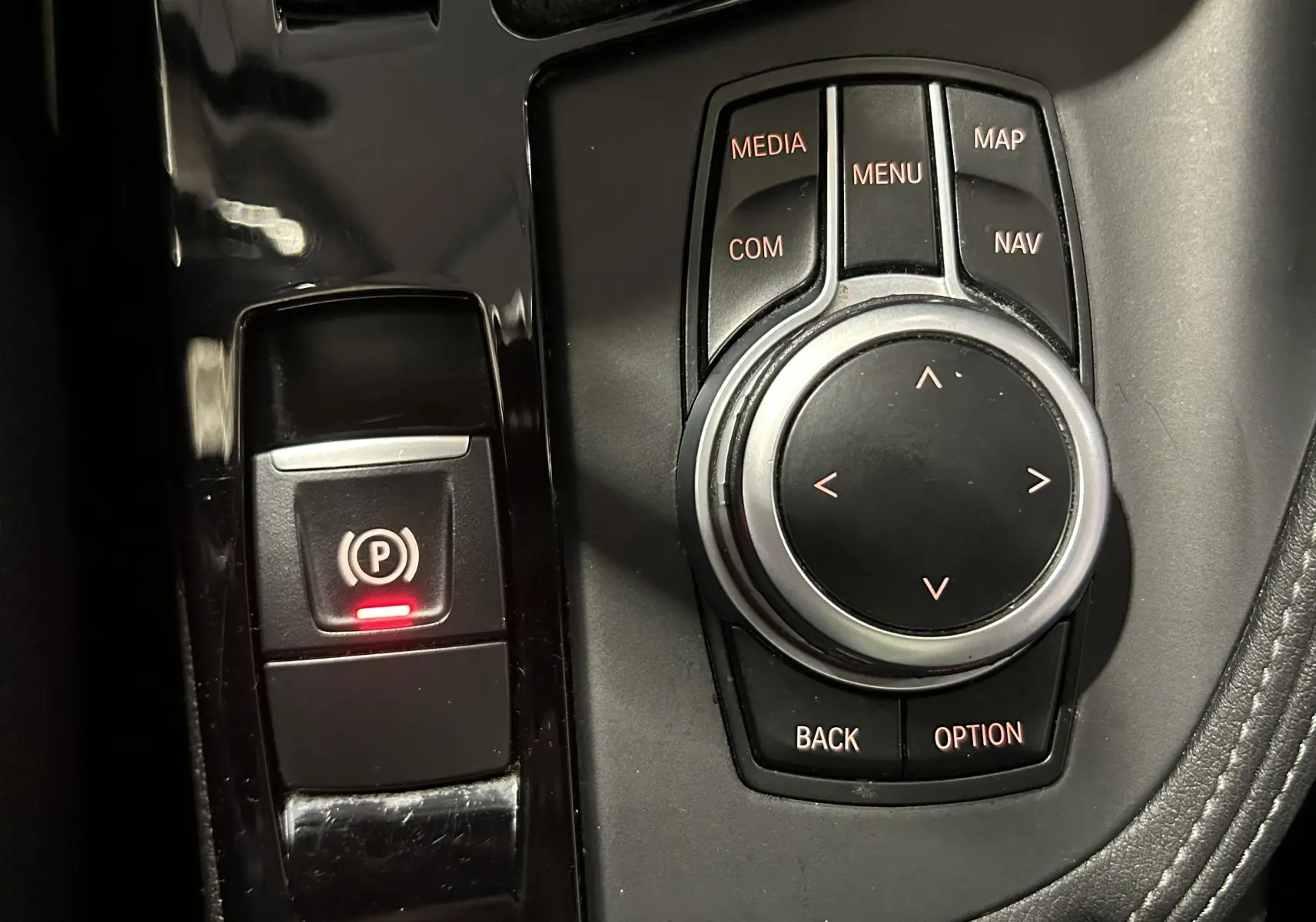 Gros plan sur la molette de commande multimédia et le bouton de frein à main électronique avec témoin rouge dans un intérieur noir.