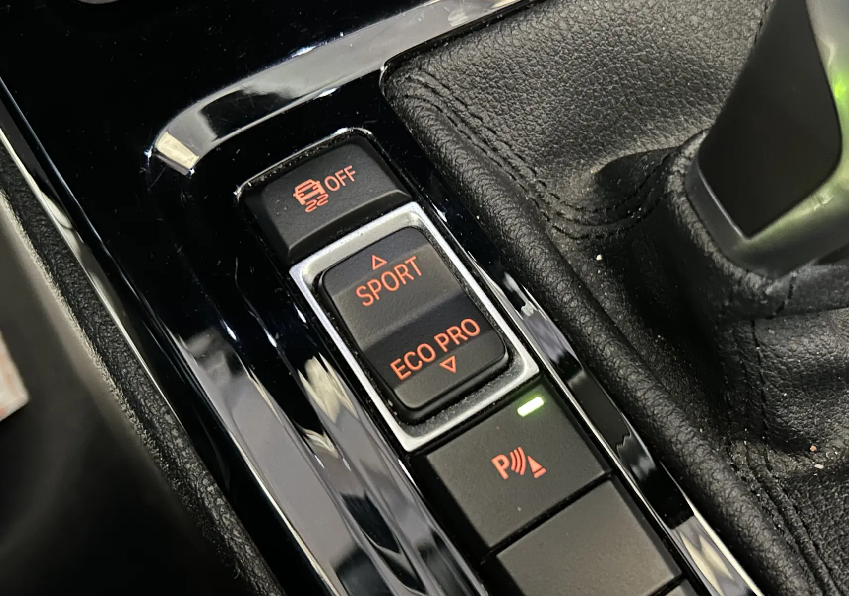 Gros plan sur les commandes de modes de conduite et assistance au stationnement dans l’habitacle d’une BMW X1 gris.