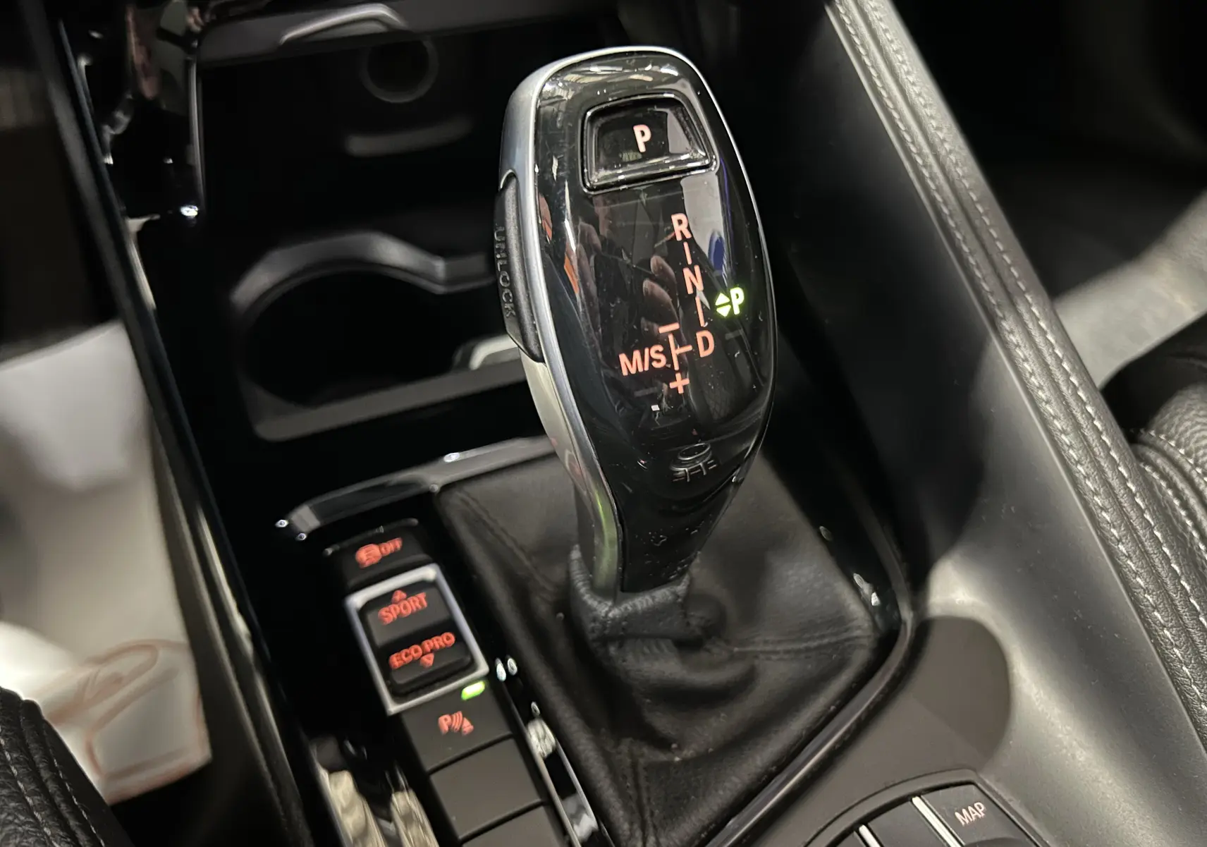 Gros plan sur le levier de vitesses automatique noir brillant et les commandes de mode de conduite dans l’habitacle d’une BMW X1 gris.