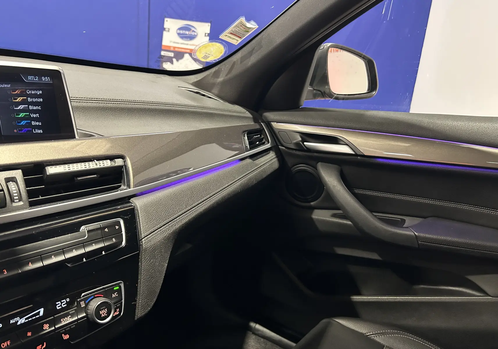 Vue intérieure côté passager du tableau de bord noir et garniture bois d'une BMW X1 gris, avec éclairage d'ambiance violet.