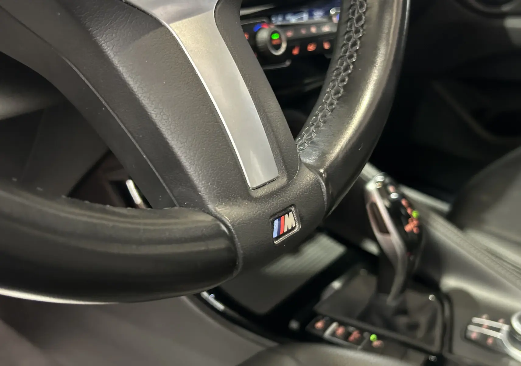 Gros plan sur le volant cuir avec logo M et levier de vitesse automatique dans l’habitacle noir du BMW X1 gris.