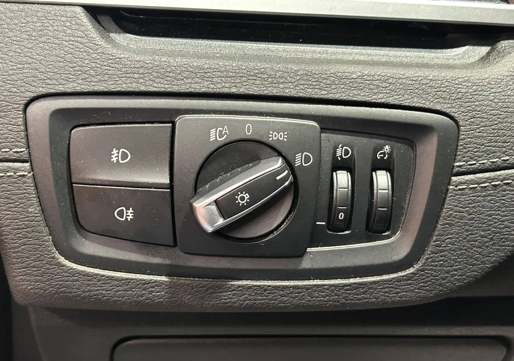 Commande des feux et réglages d'éclairage sur tableau de bord noir d'une BMW X1 gris, vue en gros plan.