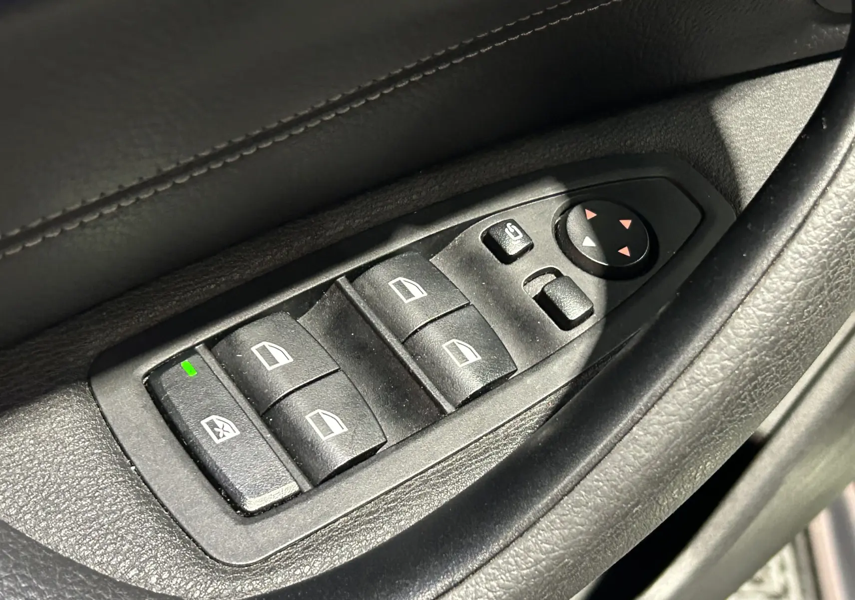 Gros plan sur les commandes de lève-vitres et rétroviseurs électriques côté conducteur d’un BMW X1 gris.