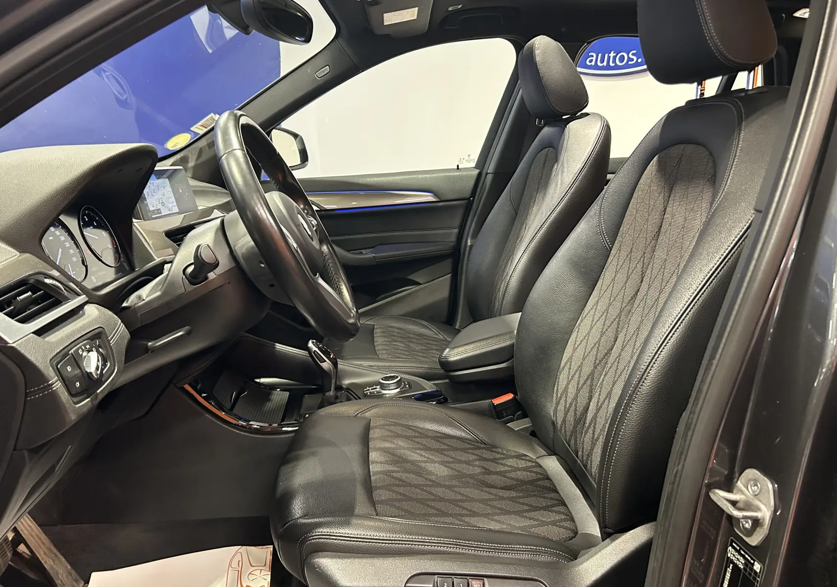 Vue intérieure côté conducteur d’un BMW X1 gris 2021, sièges avant en cuir noir avec surpiqûres et volant multifonction.