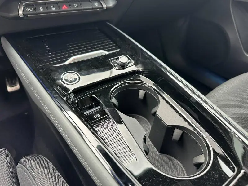 Vue rapprochée de la console centrale noire brillante de l'Audi Q3 2.0 TDI 150ch S line avec boutons et porte-gobelets.