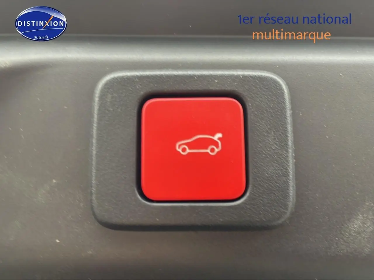 Bouton rouge de déverrouillage du coffre sur fond noir à l'intérieur du Peugeot 3008 blanc 2025.