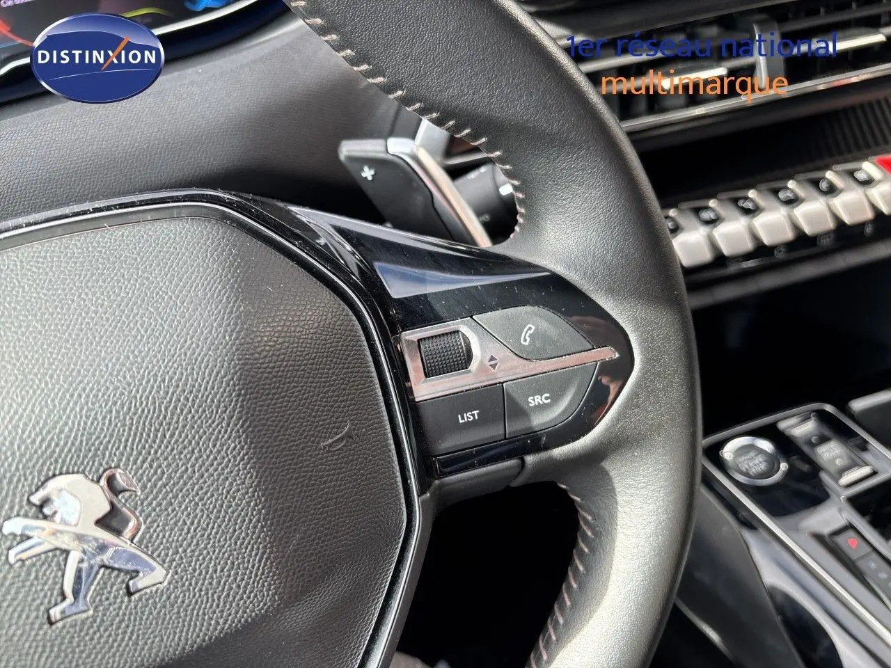 Gros plan sur le volant en cuir noir du Peugeot 3008 Hybrid 2024, avec commandes intégrées et tableau de bord partiel visible.