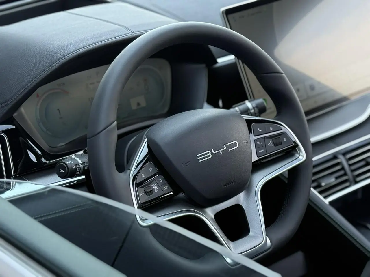 Gros plan sur le volant noir multifonction BYD avec tableau de bord digital et écran tactile à droite.