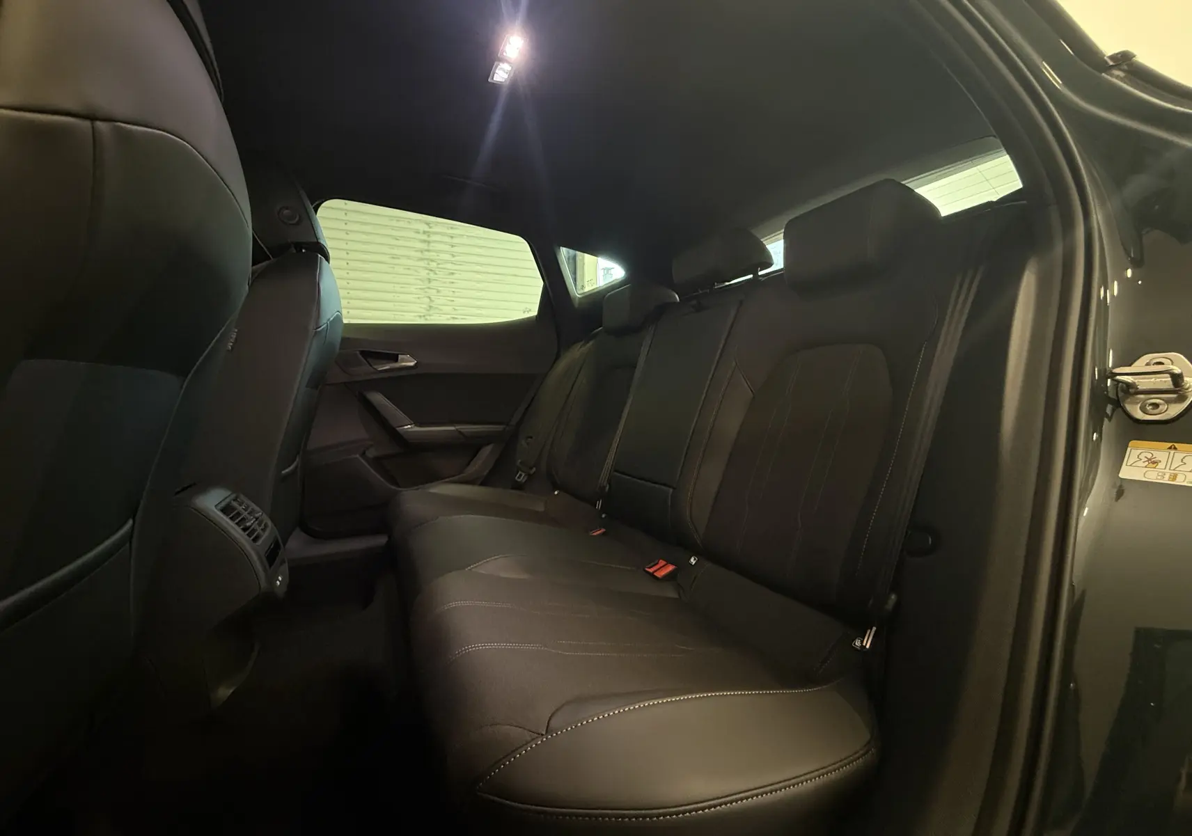 Vue intérieure arrière du CUPRA Formentor gris 2026, montrant les sièges arrière en cuir noir et la porte ouverte côté droit.