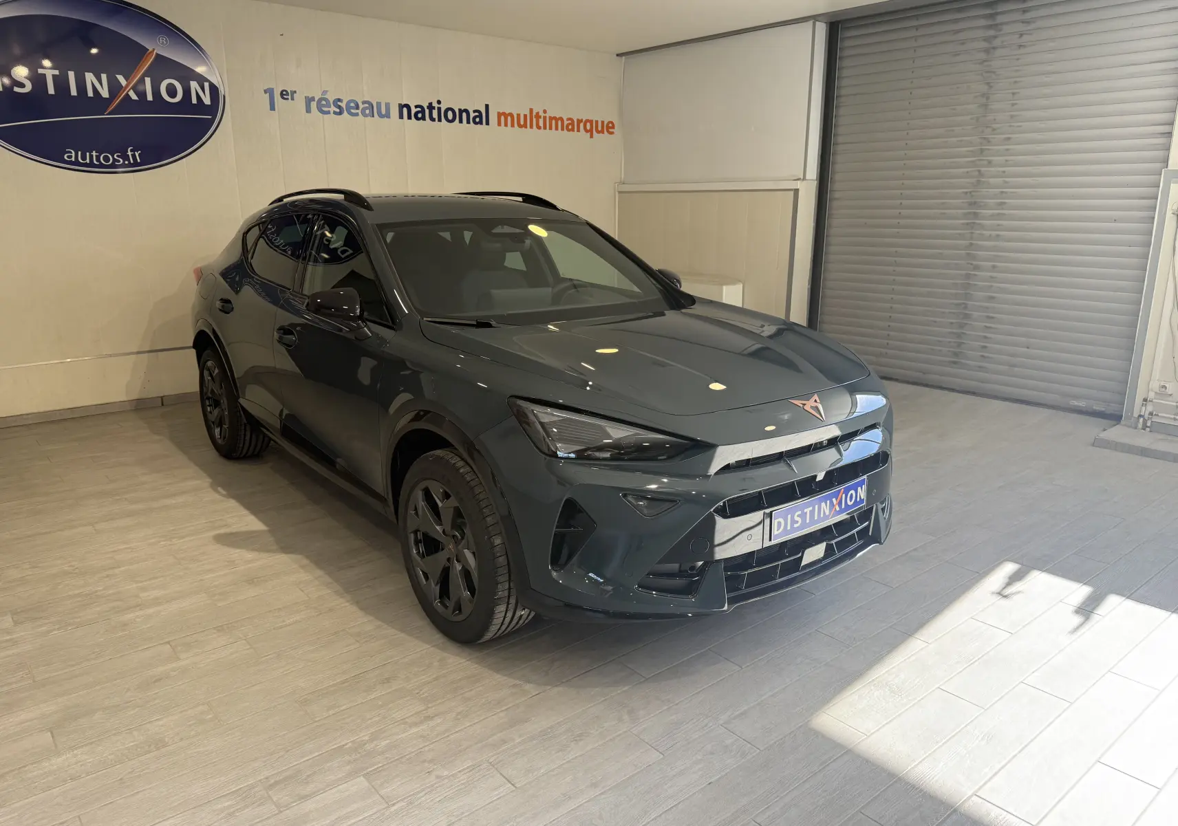 Vue 3/4 avant d'un CUPRA Formentor gris foncé 2026 avec jantes noires, dans un showroom lumineux.