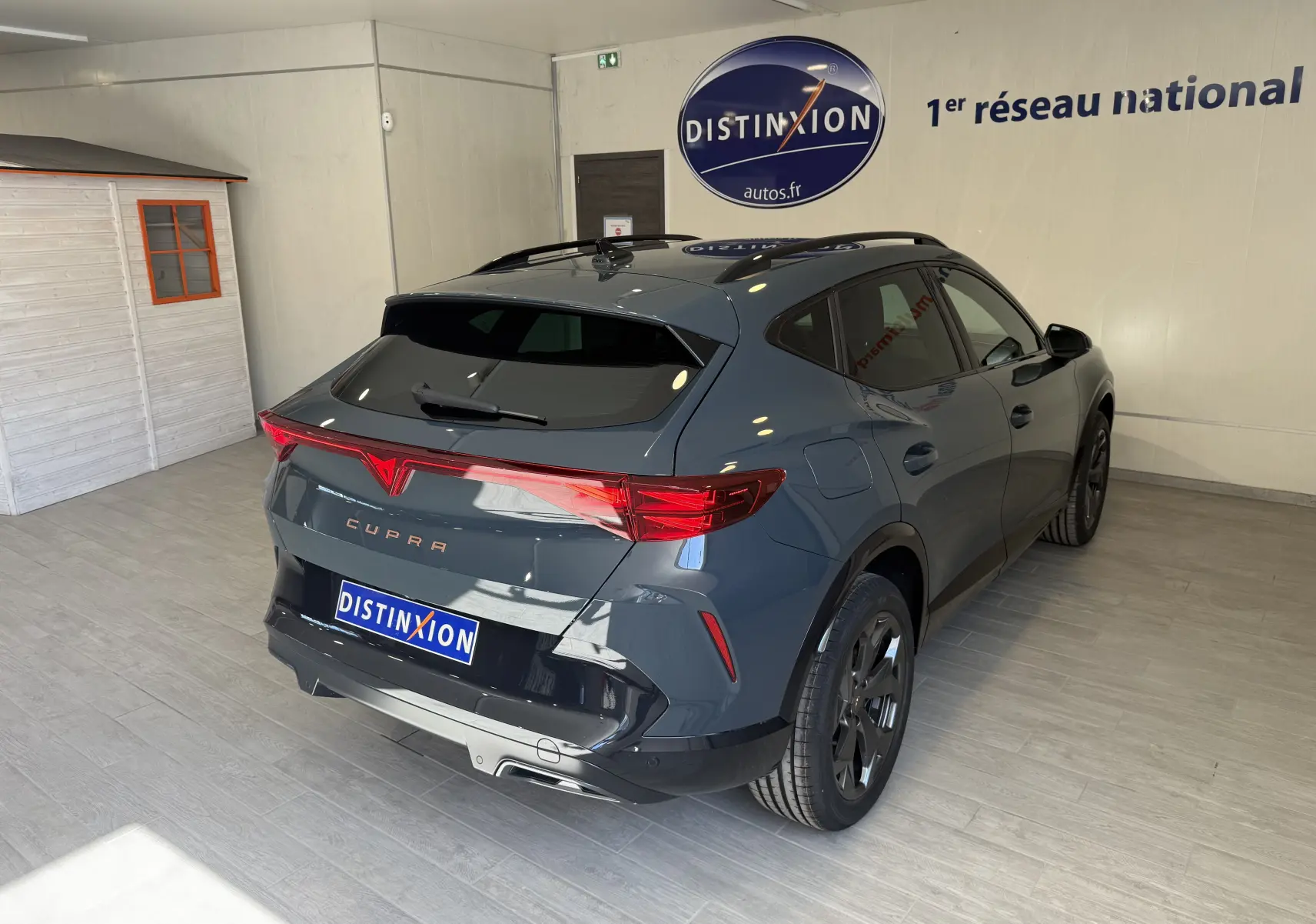 Vue 3/4 arrière droite d'un CUPRA Formentor gris 2026 avec feux arrière LED et jantes noires en intérieur showroom.