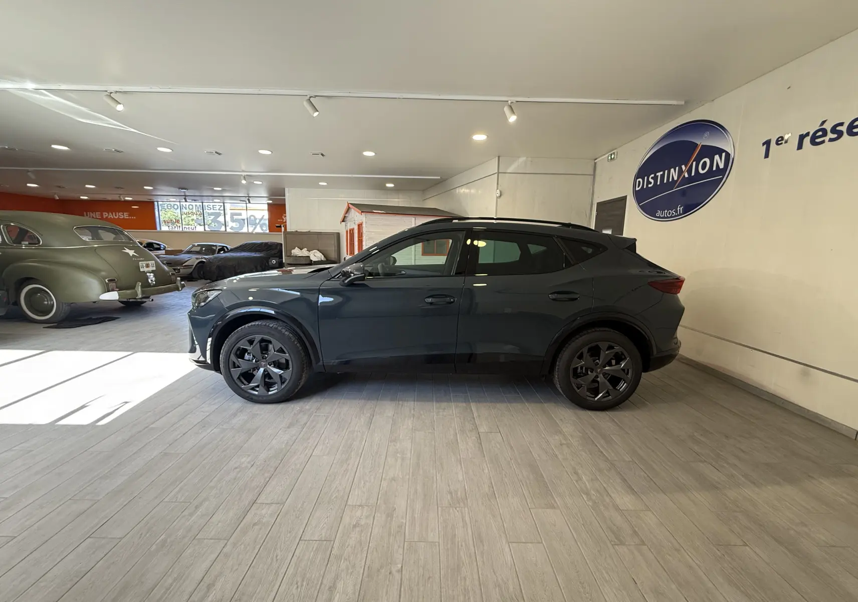 Vue de profil côté gauche d’un CUPRA Formentor gris 2026 en showroom, avec jantes noires et lignes dynamiques.